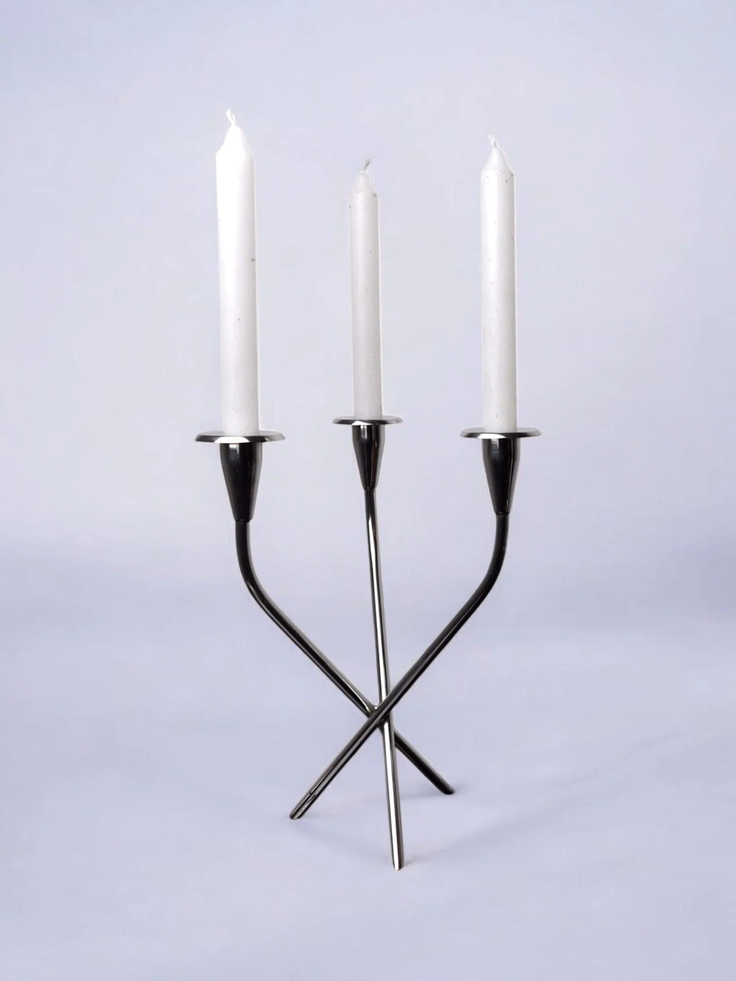 The Scandinavian Candleholder by Malamar Studio, Sweden, 1970, is a modern silver piece with three white candles. Its abstract intertwined design has vertical elements, capturing the minimalist elegance of chic Swedish decor against a light grey background.