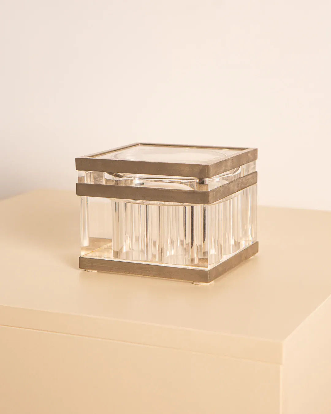 The Metal and Plexiglas box by Soldi & Scati 70's from Treaptyque, featuring a rectangular shape with metallic details and a Plexiglas body, rests on a light-colored surface, showcasing minimalist design. The box's clear sides and flat top highlight its elegance and simplicity.