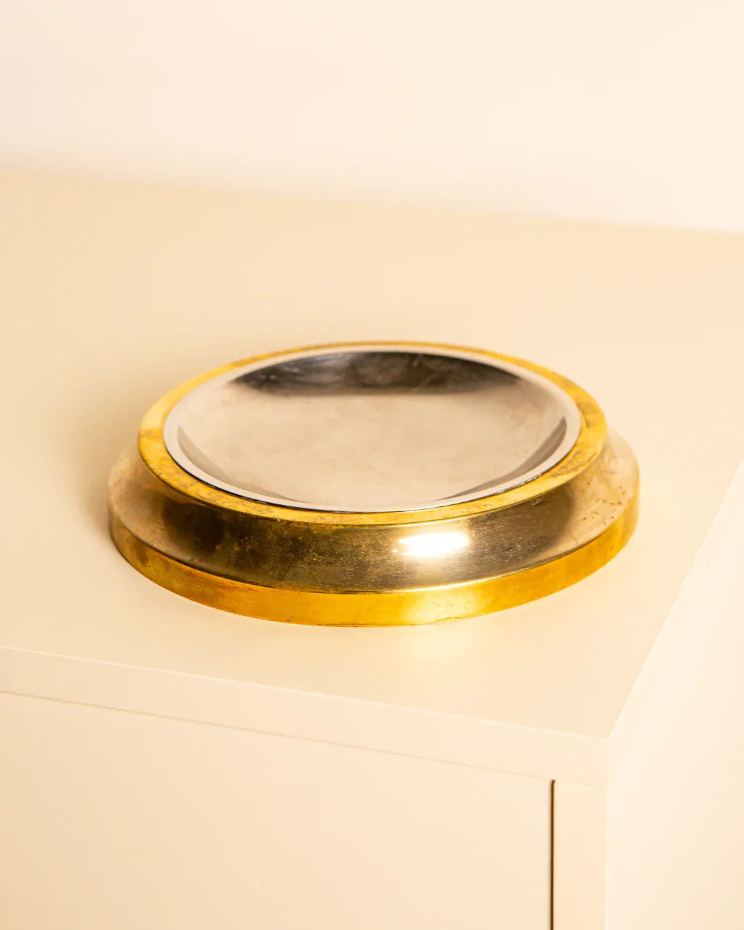 The Treaptyque Vide-Poches in 60's Brass is a shallow, reflective metal bowl with a wide golden rim, exuding vintage charm and sophisticated design, sitting on a light-colored surface against a plain background.