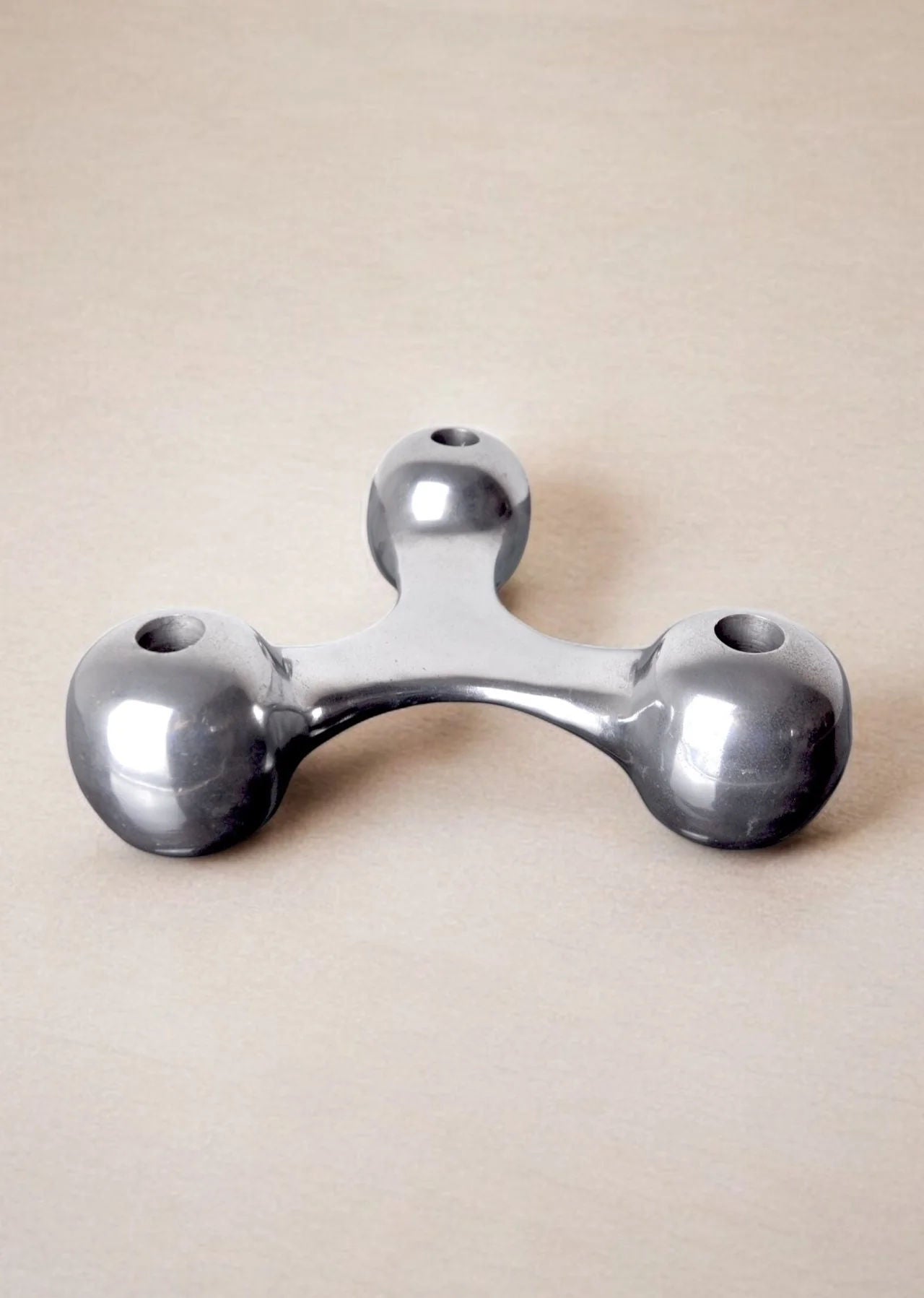 A metallic, triangular Scandinavian Candleholder from Malamar Studio, Denmark, 1970s, rests on a light surface. Each of its three aluminum knobs features a circular indentation on top, creating an exquisite design object.