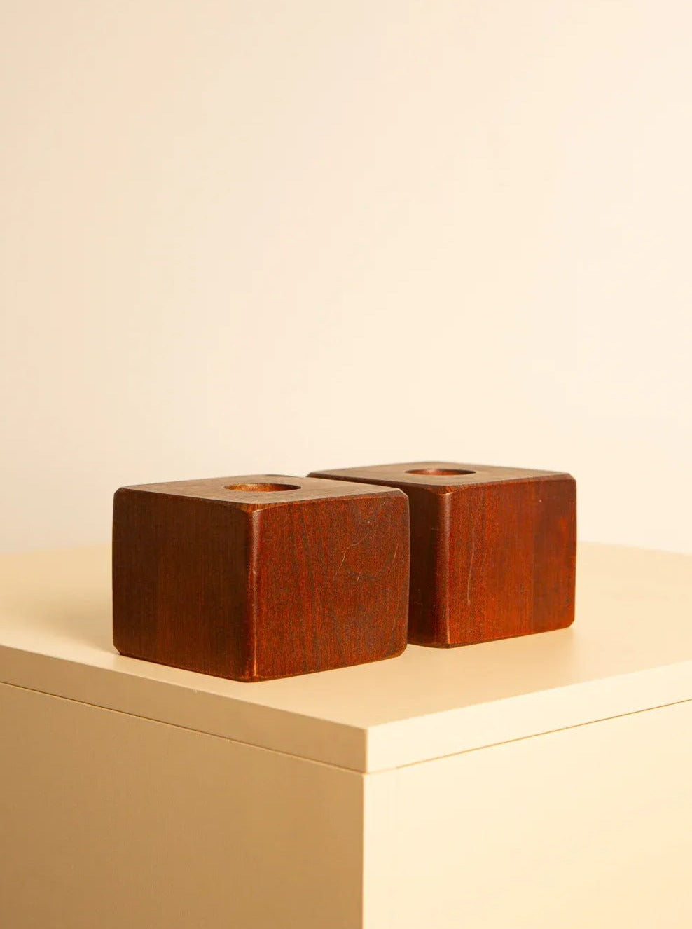 Two vintage wooden candleholders, cube-shaped with holes in their centers, sit on a light-colored table against a plain background. The Italian craftsmanship is evident, suggesting they may function as elegant candle holders or similar decorative items. These are the Pair of Cube-Shaped Wooden Candleholders 80's by Treaptyque.