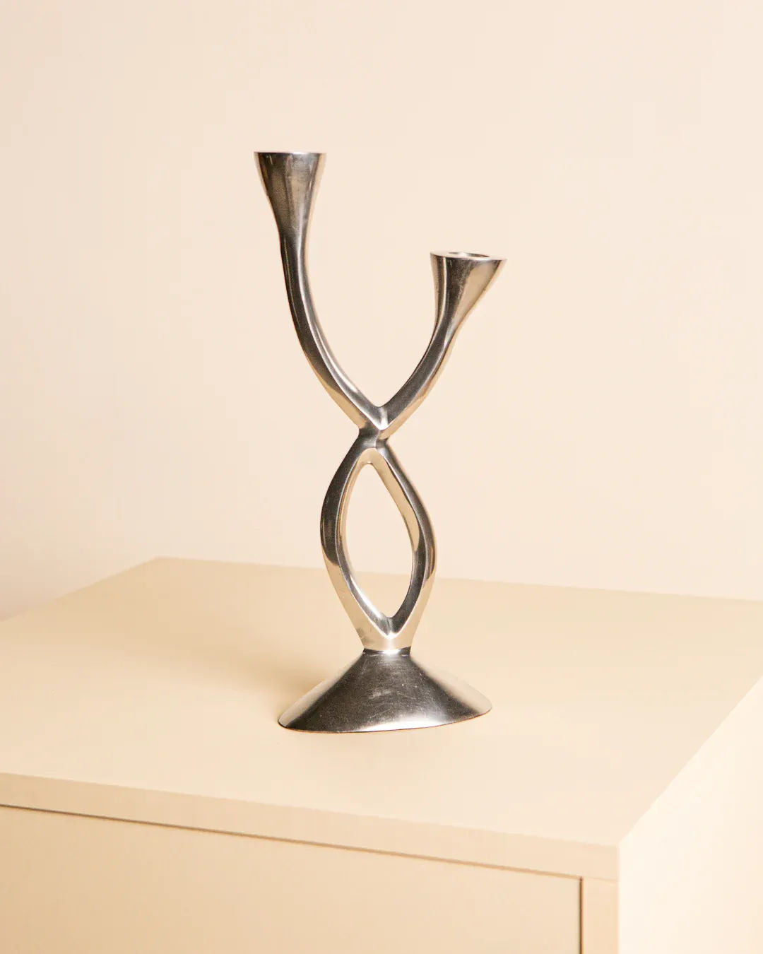 The Candleholder in Aluminum "Torsadé" 80's by Treaptyque features a modern, silver design with twisted aluminum and two upward-facing arms. It stands elegantly on a light-colored rectangular surface against a plain beige background, exuding '80s charm.