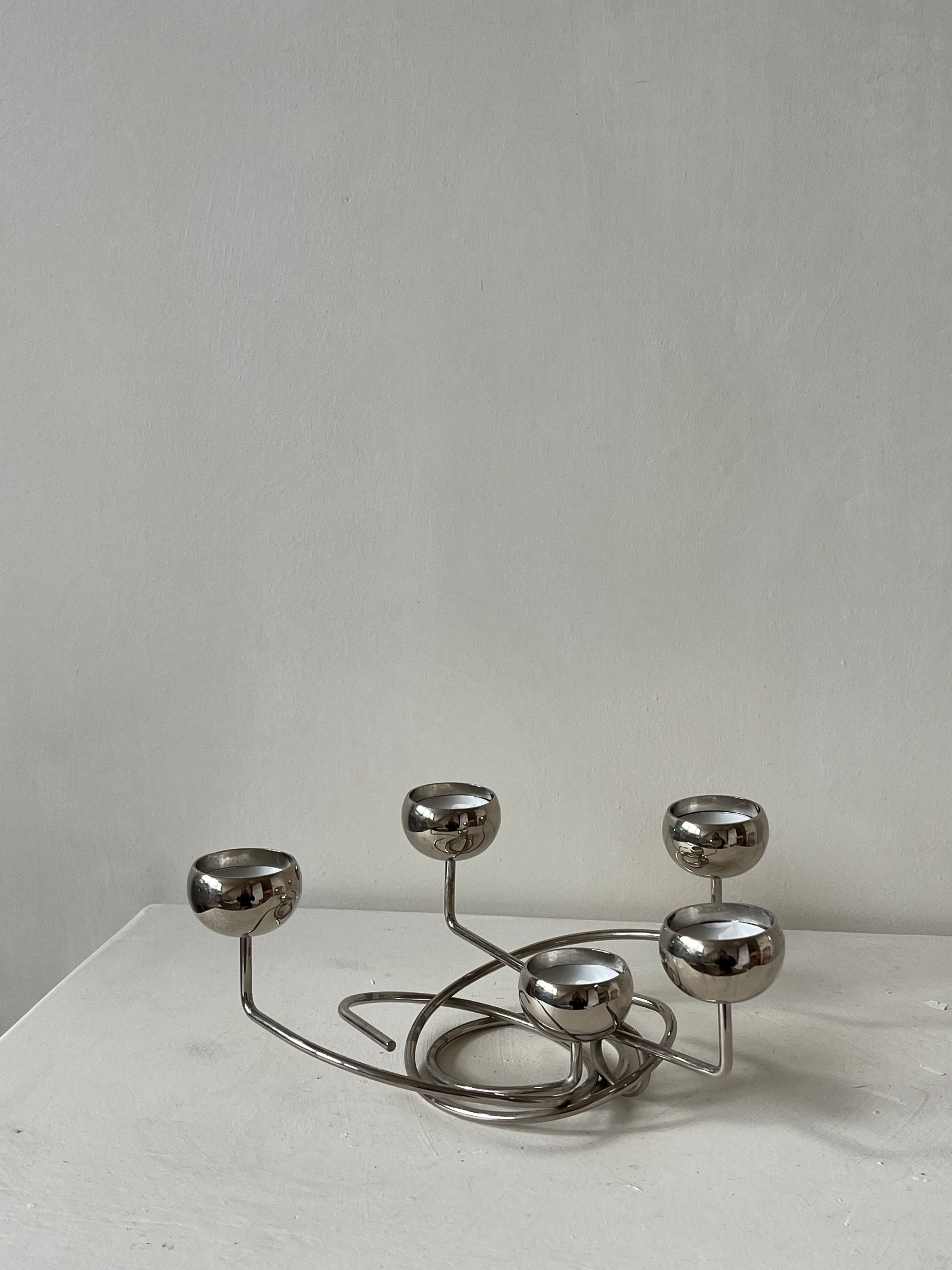 Introducing the Chrome Candleholder by septembre studios: a modern, sculptural piece featuring five rounded holders on an elegantly intertwined base. Its unique angles stand out beautifully against a plain gray background on a white surface.