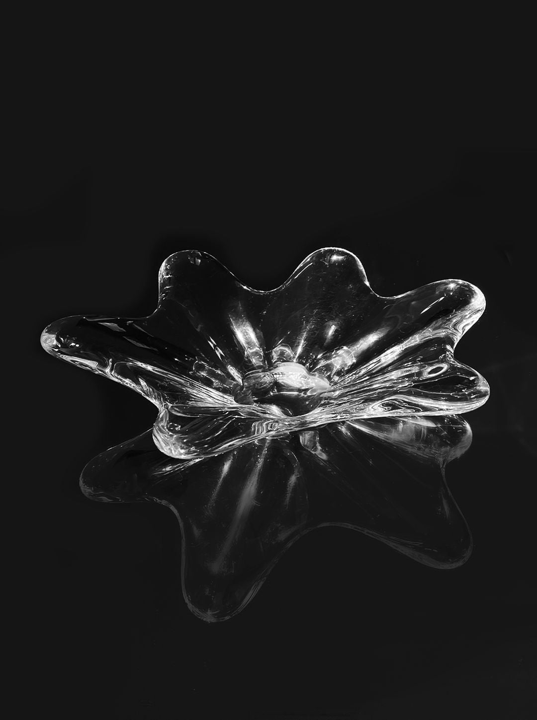A wavy, transparent Les Objoies Crystal Baccarat Cup graces a black background, its shape mirrored below. The design evokes gentle waves or petals, forming an elegant and modern vessel that highlights exquisite crystal artistry.