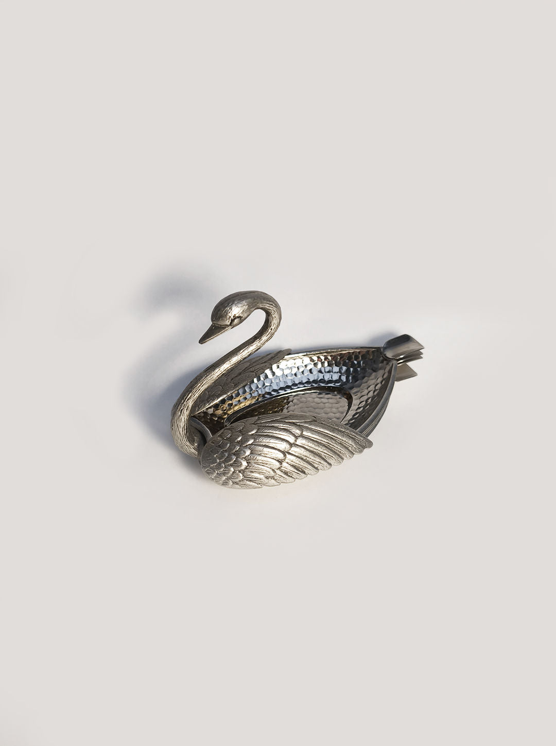 The Les Objoies Swan Ashtray, made of silver-toned metal, features elegantly curved designs with a textured body on a light gray background. Its wings have a scale-like pattern, seamlessly blending style and function for chic smoking areas.