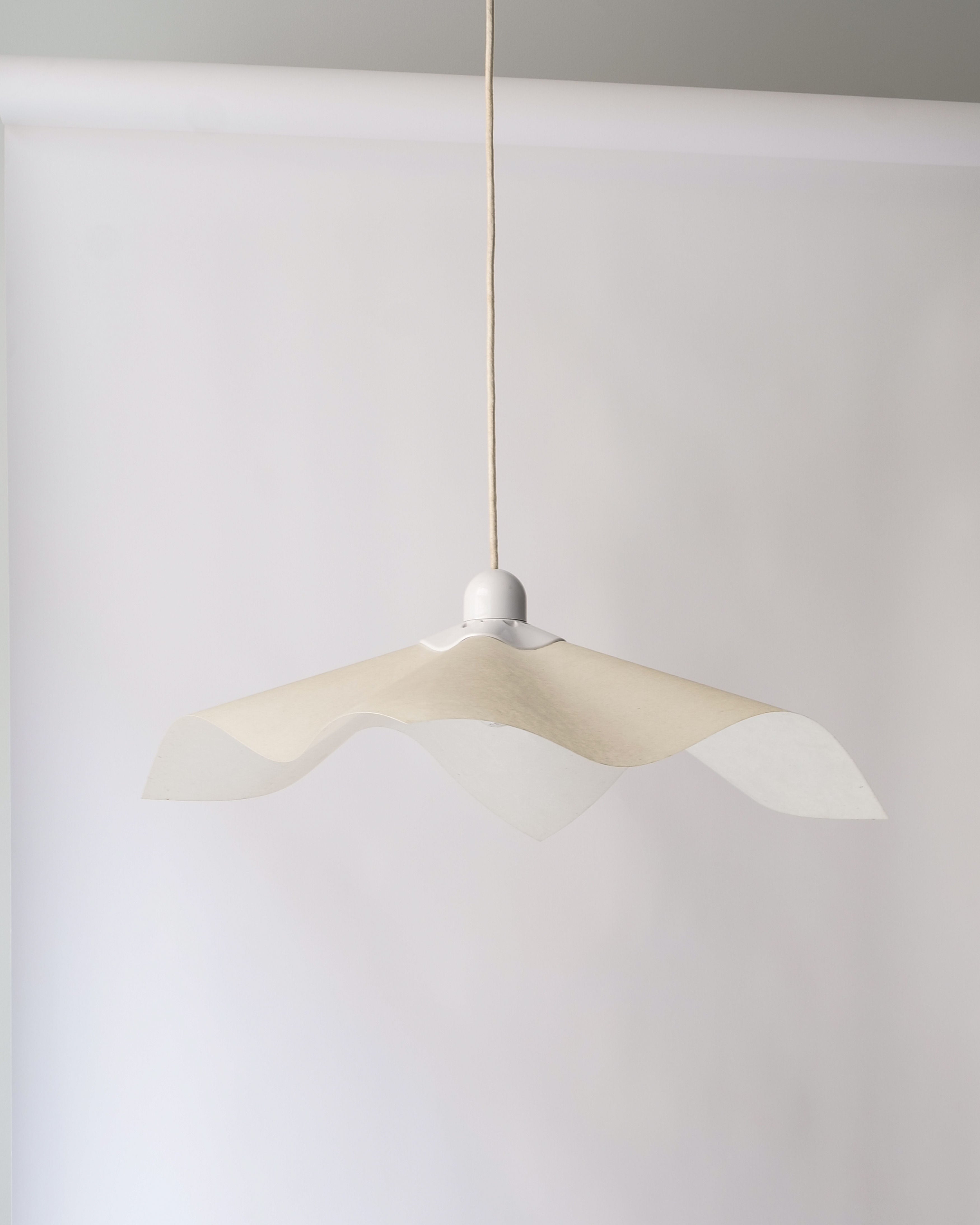 The Adjustable Ceiling Lamp Mario Bellini 1970 by Collection apart features a modern pendant with a wavy, translucent white shade, echoing 1970s Italian design, against a plain gray background.