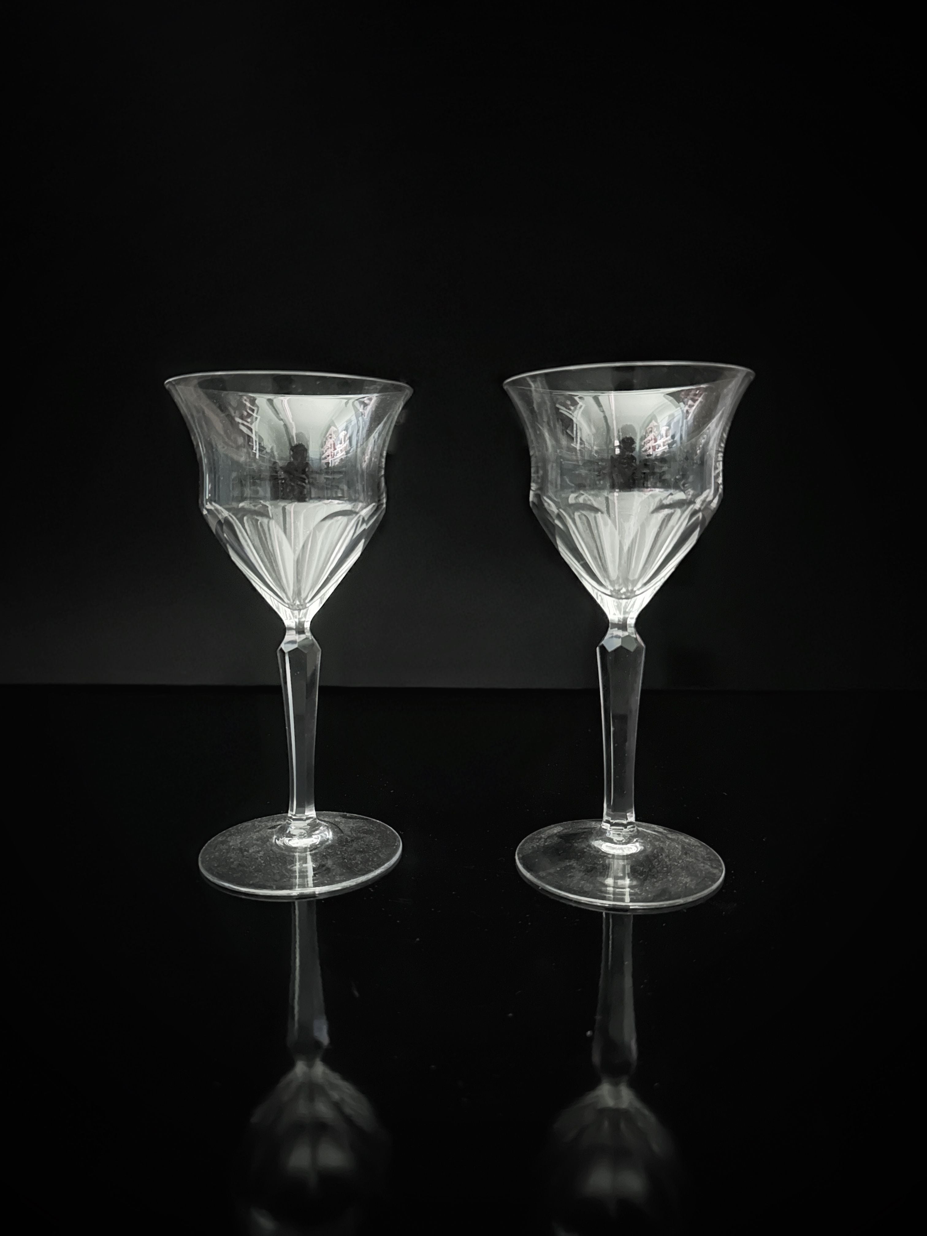 Two stunning Dodo Vintage hand-cut crystal wine glasses from the 1960s are elegantly displayed on a reflective black surface, set against a dark background.