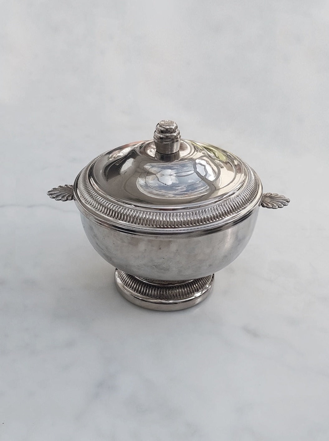 A white ceramic sugar bowl with a lid and spoon on a kitchen countertop