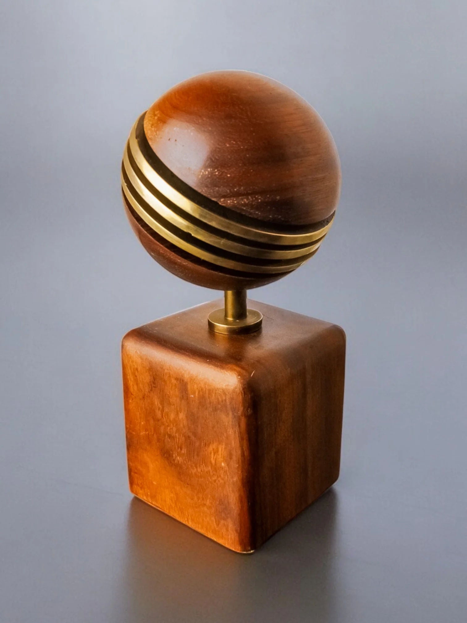 The Brutalist Paperweight by Ardisur, Spain 1970 for Malamar Studio features a wooden sculpture of a sphere with gold bands on a small pedestal set on a square wooden base, against a gray background.