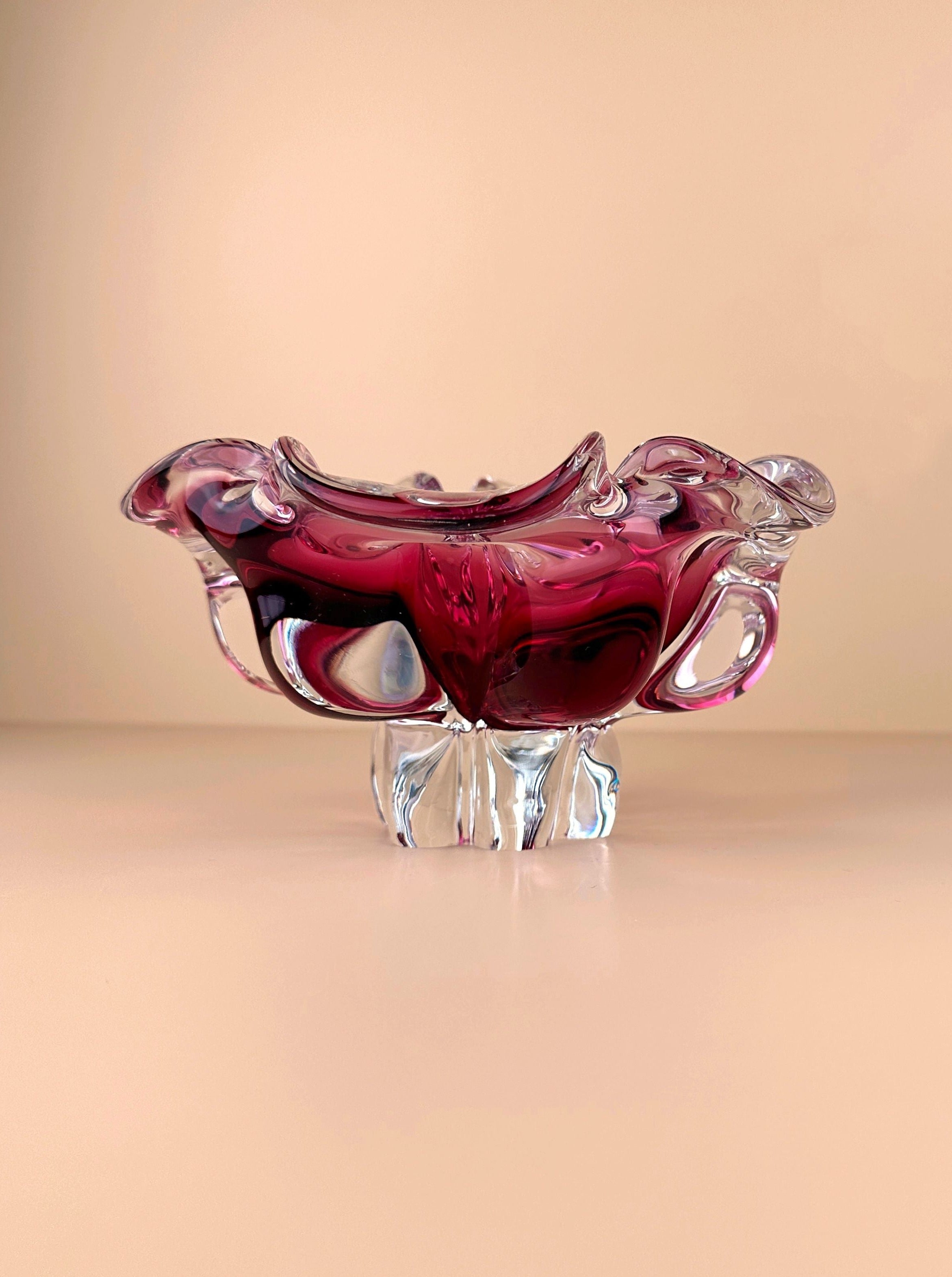 A delicate, ornate Bohemian Cranberry Red bowl by Josef Hospodka with a deep rose-colored upper section and a clear, textured base, presented against a soft beige background from Dodo Vintage.