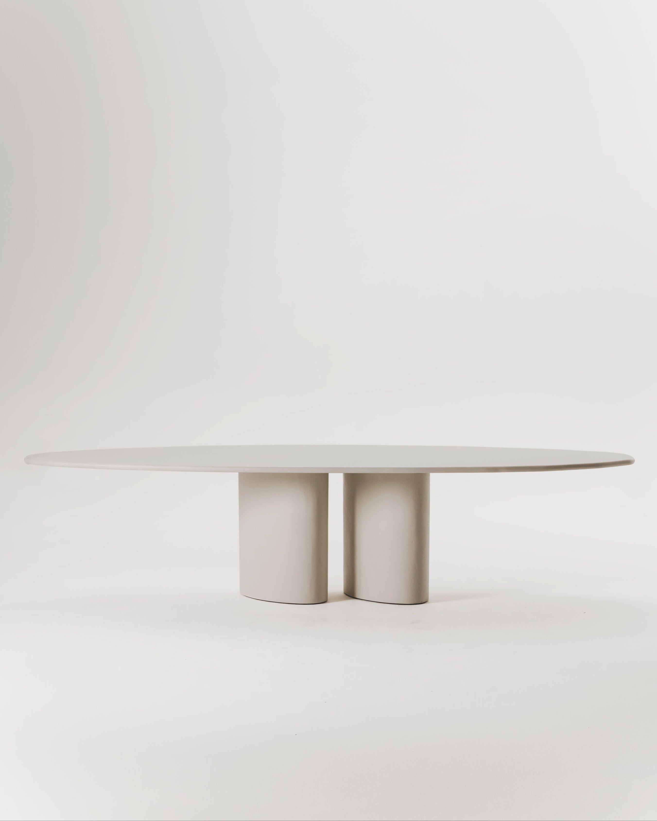 Modern oval dining table with dual cylindrical concrete pedestals in neutral beige