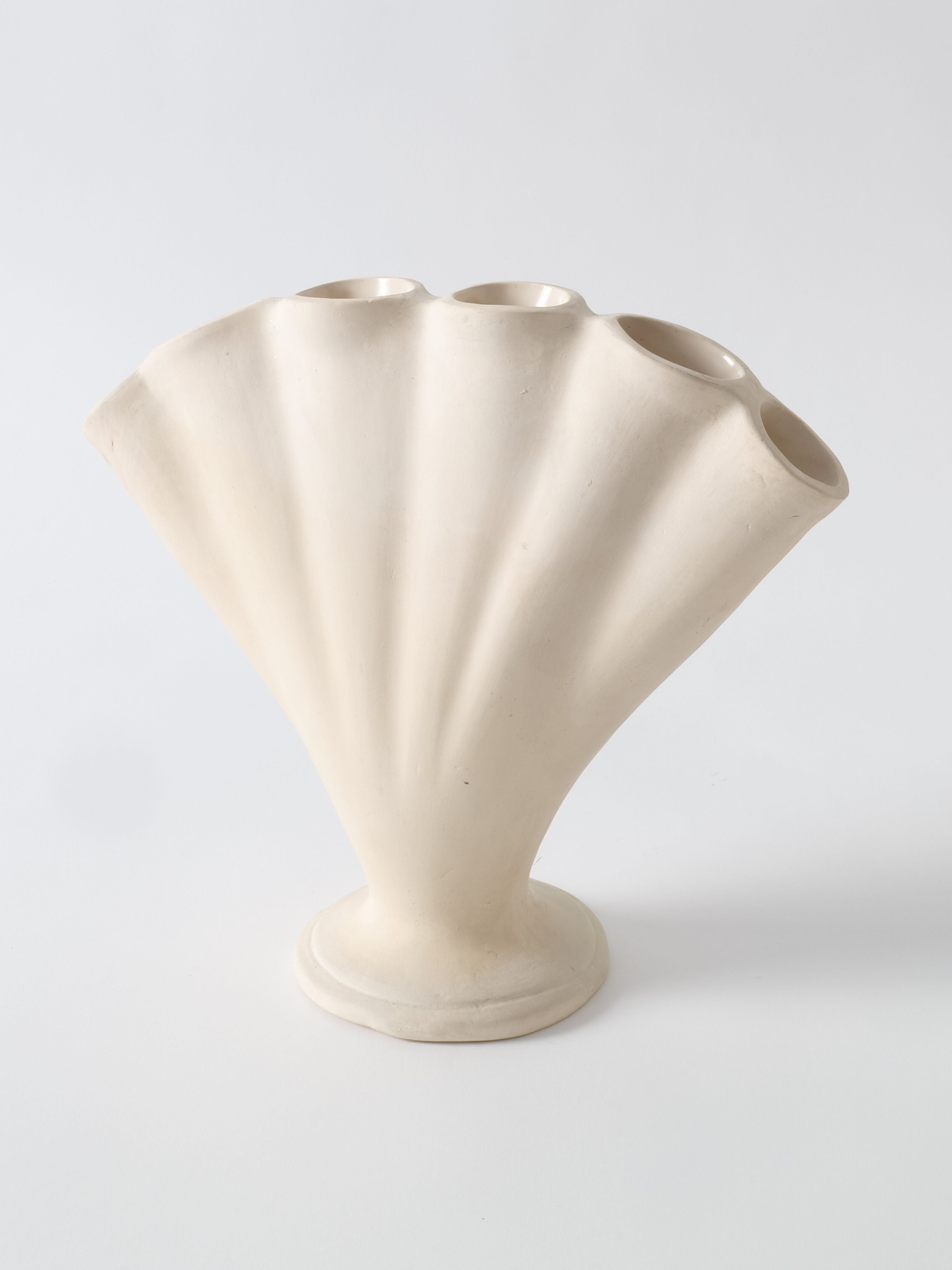 A sculptural, off-white ceramic vase with a unique design resembling a fan or seashell, reminiscent of Fulham Pottery's artistry. Known as the Tulipiere Vase 1930s by Collection apart, it features multiple openings at the top, creating an organic and artistic appearance. The vase sits on a small, round base, and the smooth matte surface evokes the elegance typically associated with tulipieres.