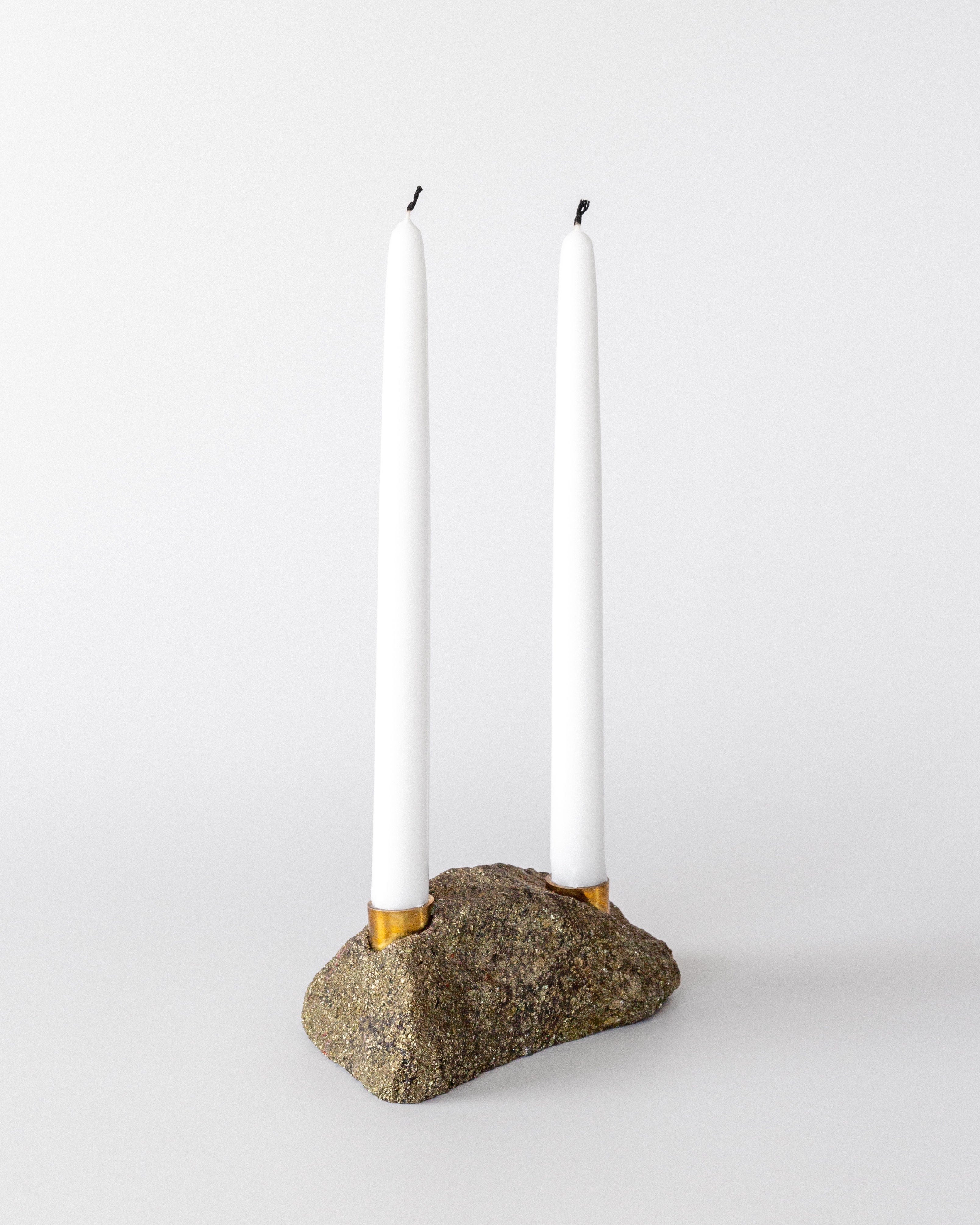 Two white taper candles stand in a Spigel Brutalist Stone and Brass Candleholder, 1970s, featuring gold holders embedded in rough natural stone, set against a plain white background.