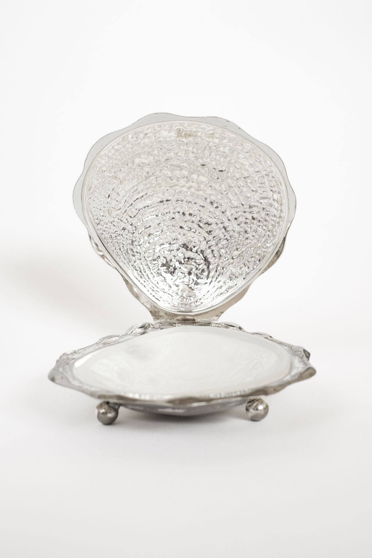 The septembre studios Shell Butter Dish features a vintage silver scallop shell shape with a textured, hinged lid, smooth white interior, and three round feet, displayed on a plain white background.