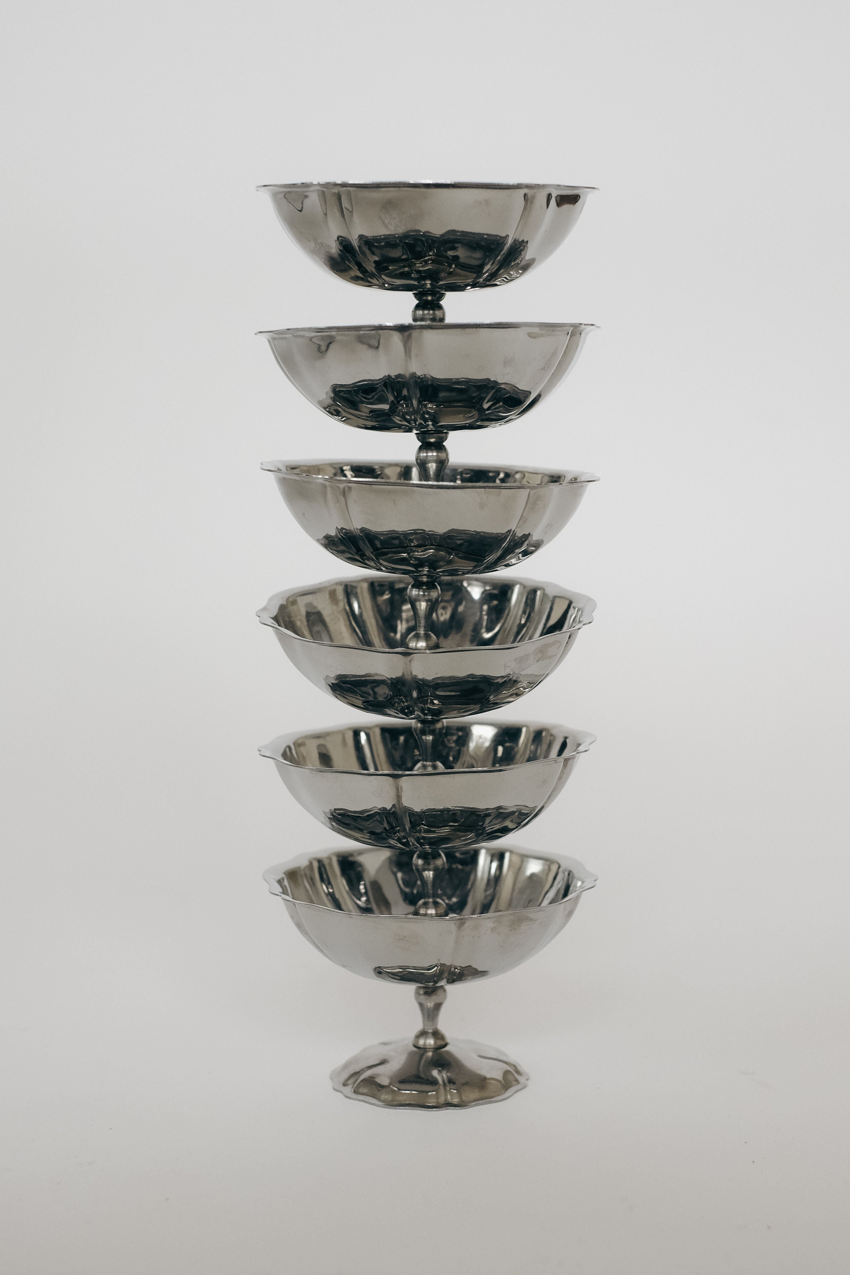 A visually striking, polished stainless steel set of "six ice coupes" by septembre studios is stacked on a plain white background, creating an elegant display—ideal for serving sophisticated ice cream treats.