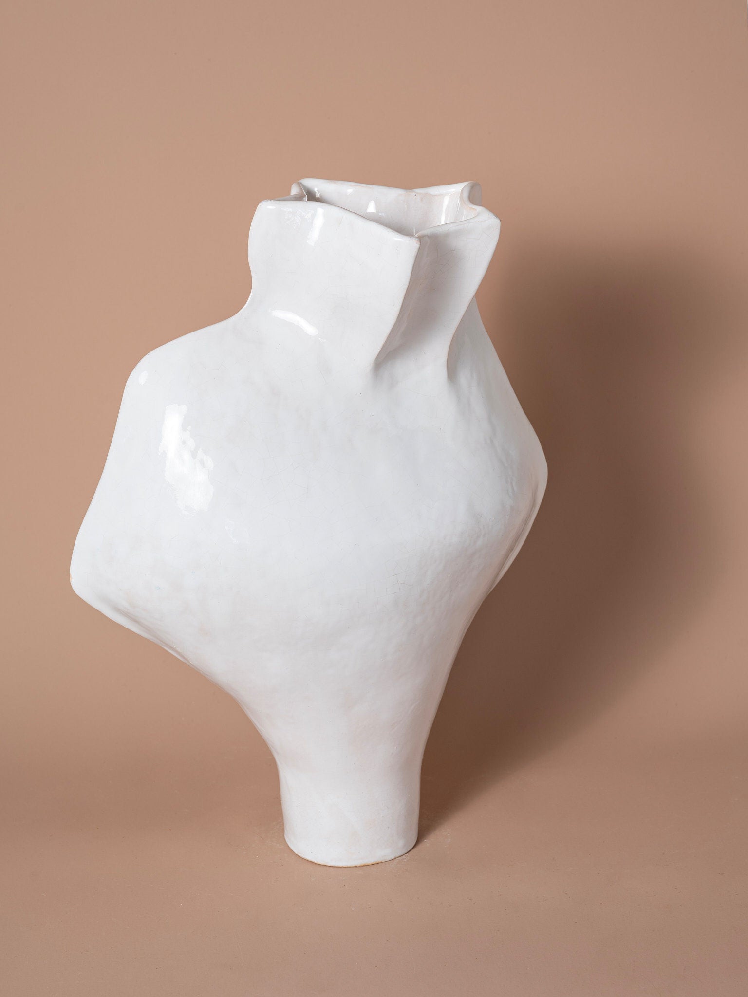 The Seed of Light Form Vase 14 from Siham Djebbar Ceramics’ Seed Series features a glossy, abstract white ceramic design with an asymmetrical shape, displayed on a neutral beige background.