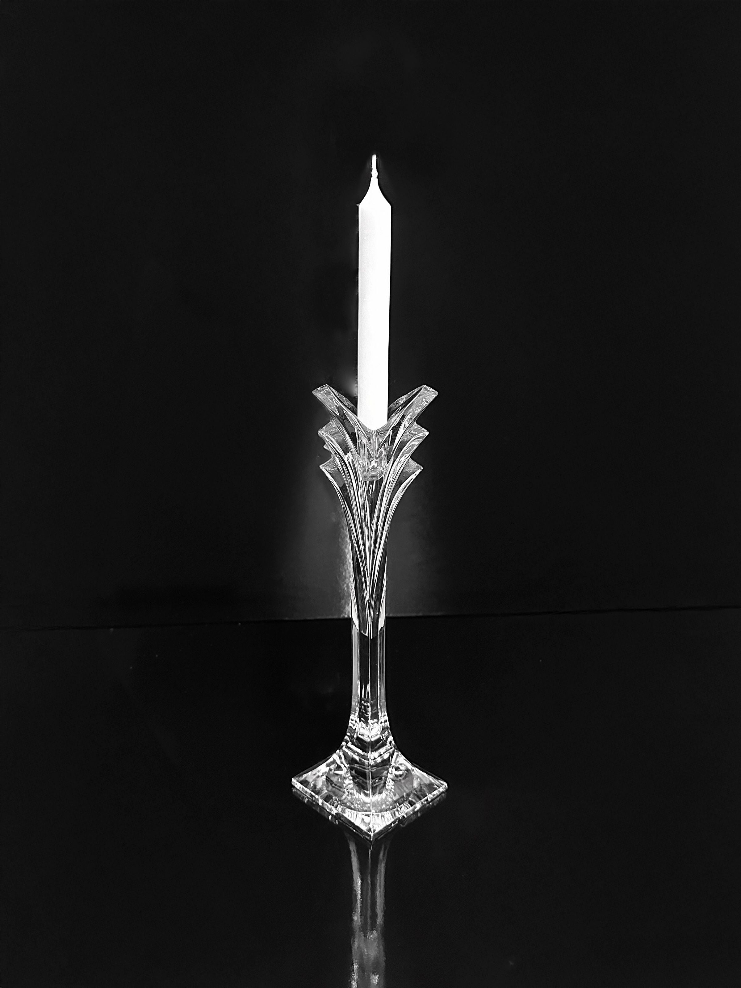 The Dodo Vintage Crystal Glass Candleholder - Nachtmann 1980s, elegantly crafted with intricate Art Deco Revival designs, holds a lit white candle. It stands on a reflective black surface against a solid black background, capturing the candle's soft glow and timeless sophistication.