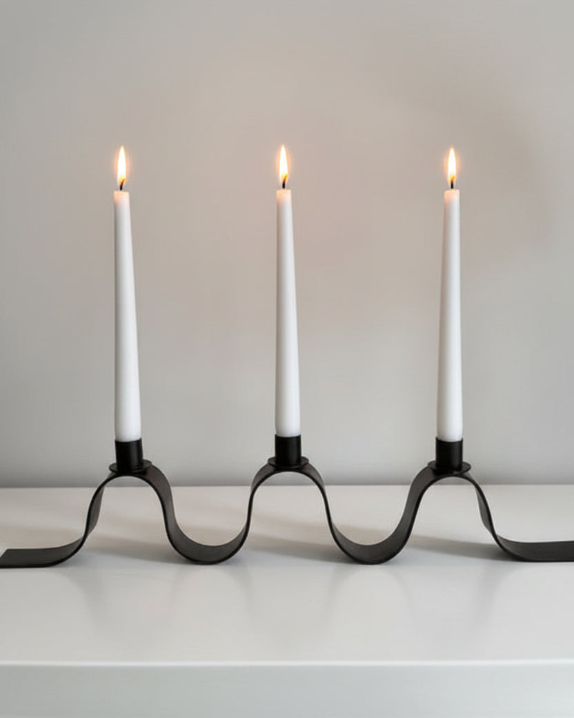 Black metal ribbon candelabra with three lit white tapered candles