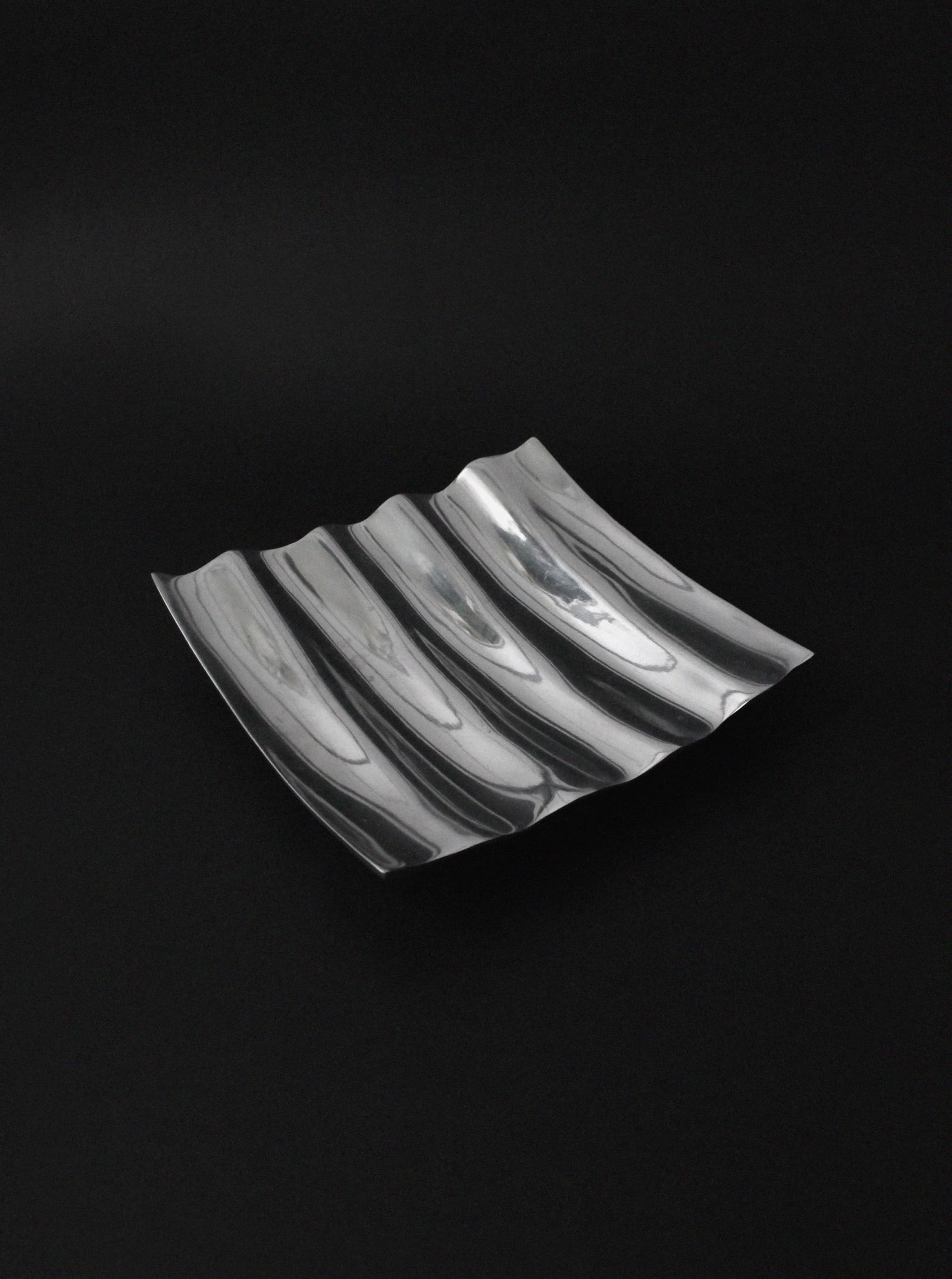 Polished aluminum wave bowl with curved ridges on black background