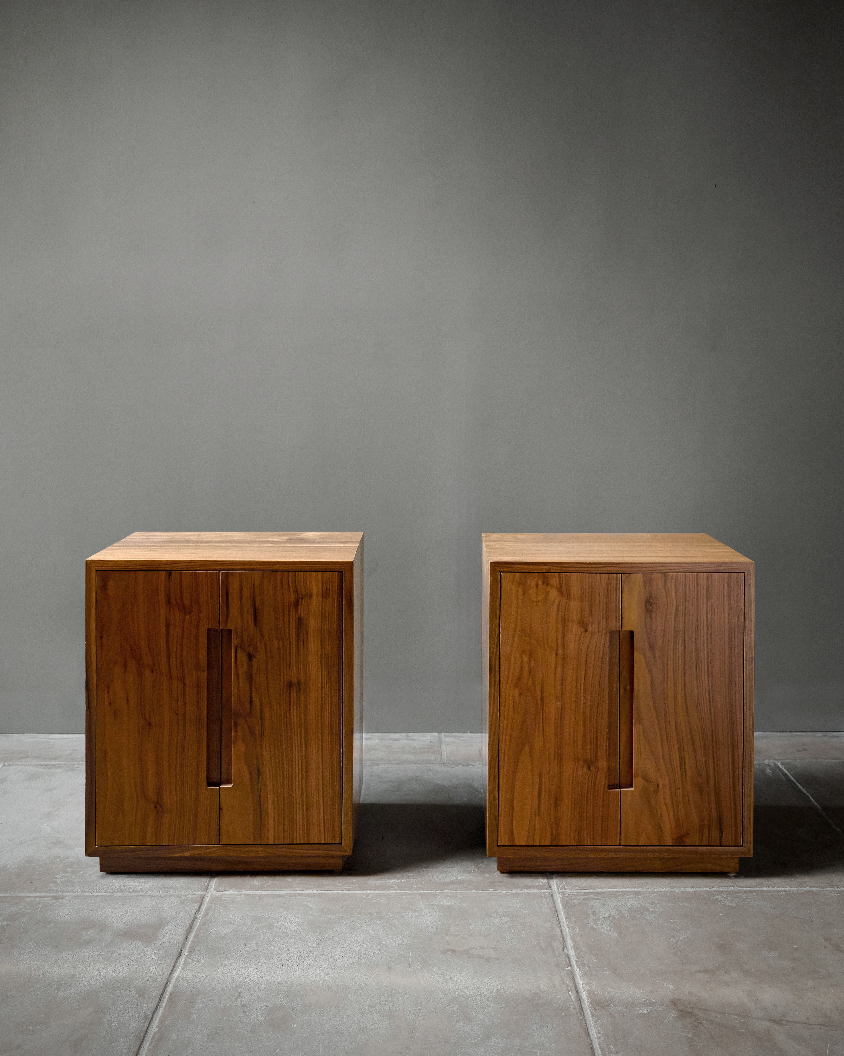 A pair of 'Bahia' Nightstands by Studio OSKLO, featuring a simple, modern Brazilian mid-century design, stand side by side on a tiled floor. Each walnut piece has a rectangular shape and vertical recessed handle on the front.