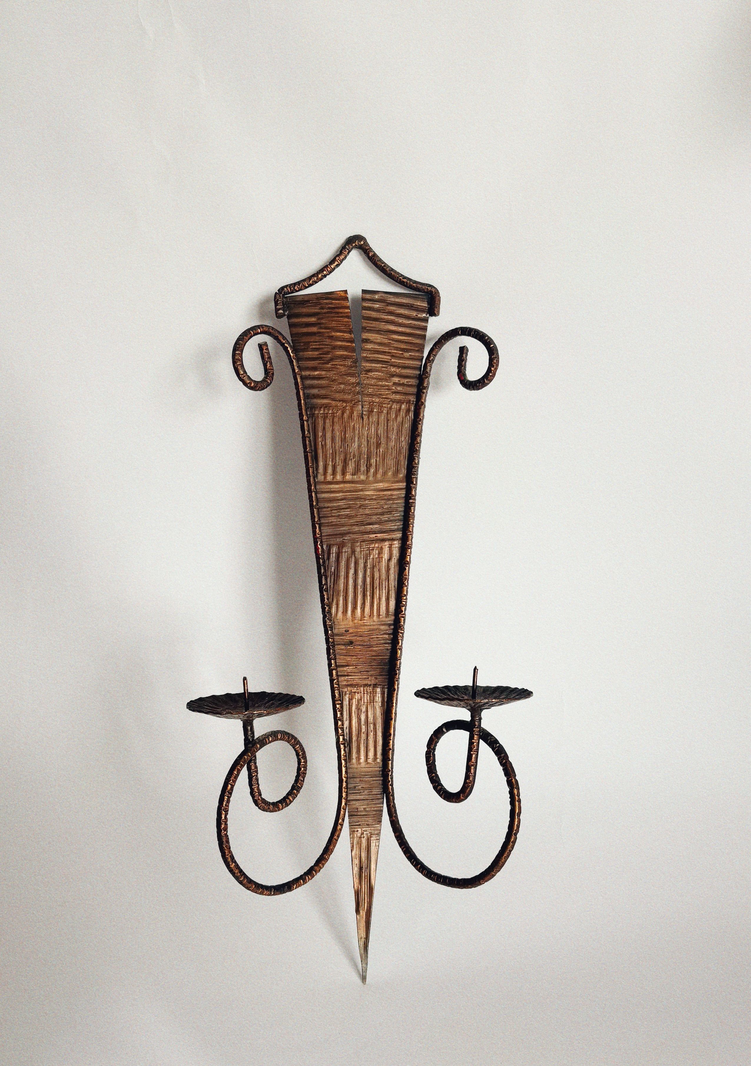 The Huerto Metalwork Wall Candleholder features a pointed, textured body, two curled arms with flat round holders, artisan design, and hammered details, displayed against a plain white background.