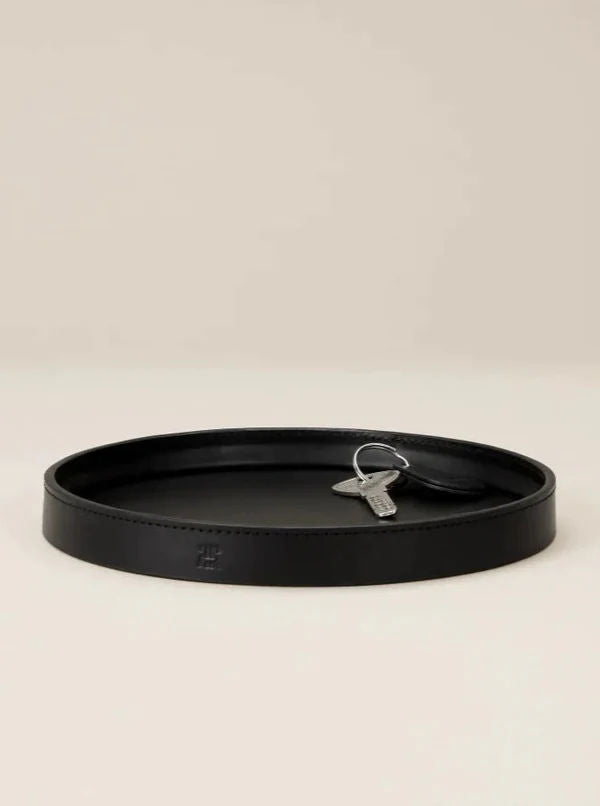 The Paradise Row Leather Trinket Tray, featuring exquisite craftsmanship, sits elegantly on a neutral background and holds a single silver key.