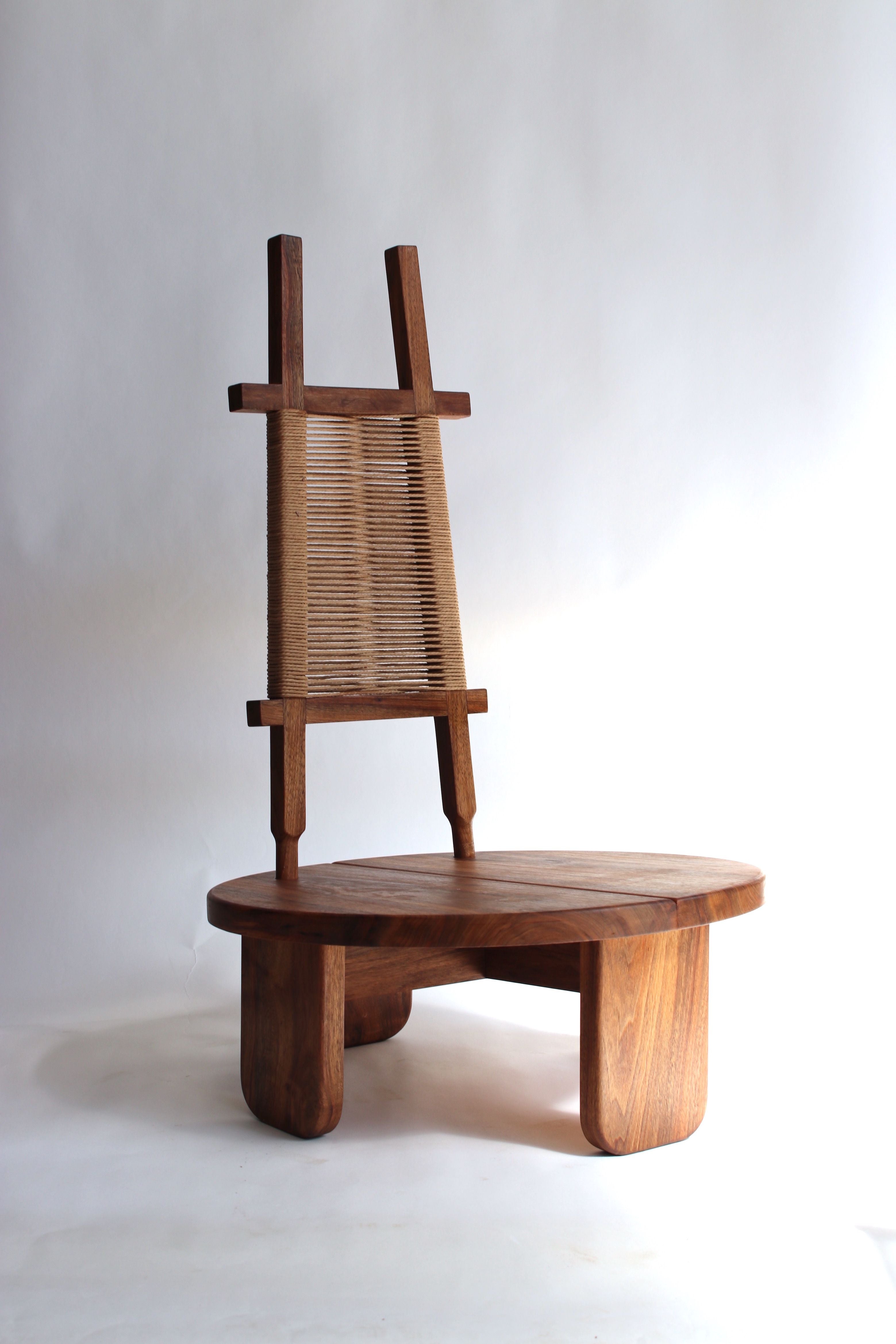 The 'Wilson' Walnut-Rope Chair by Assemblage SAS exudes minimalist charm with its wooden design, low seat, and vertical string backrest. An artisanal piece with a natural walnut finish, it stands elegantly against a plain white background.