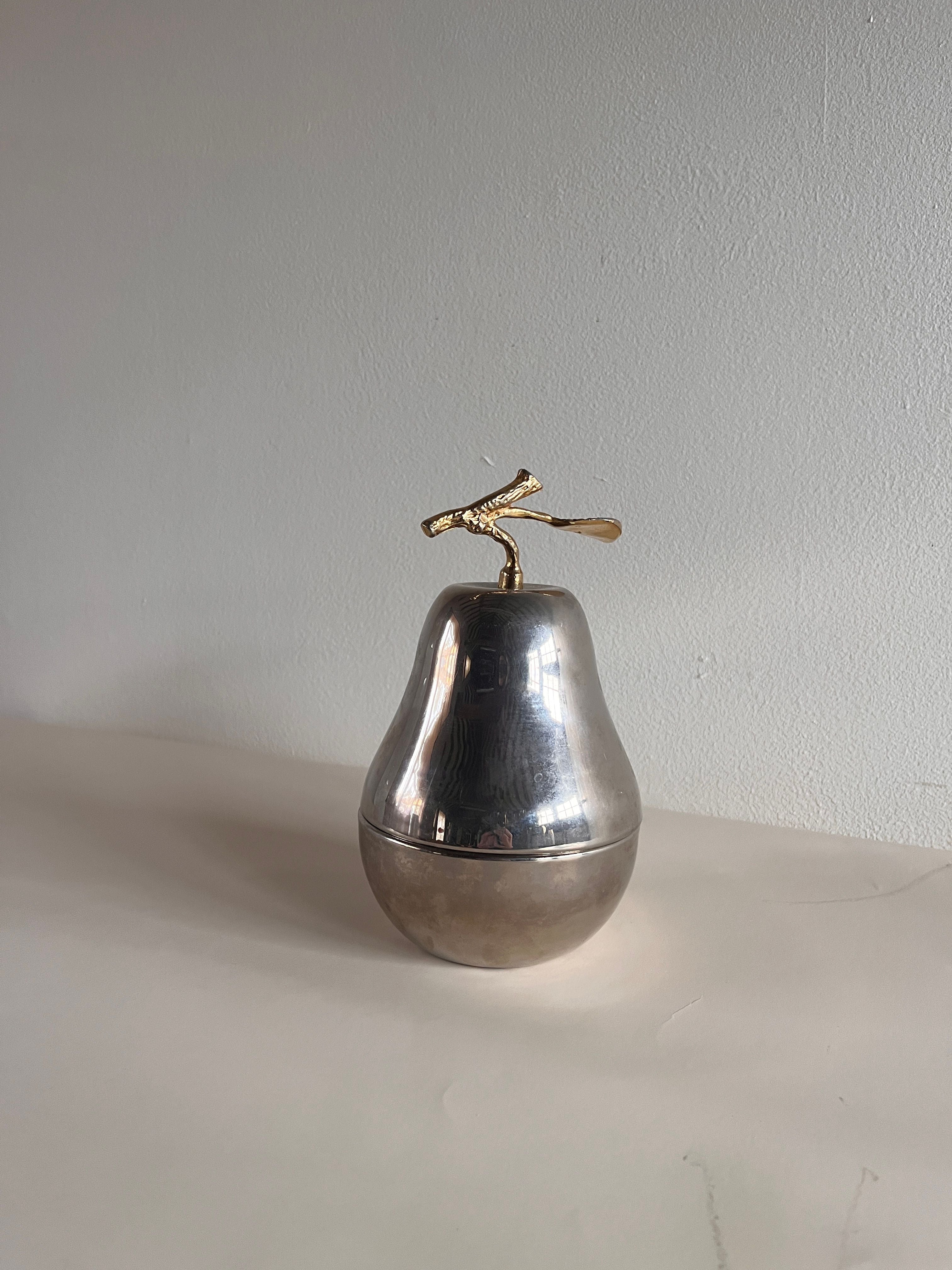 The Maud Vaughan Mid Century Pear Lidded Box, crafted as a silver container with a gold stem, elegantly rests on a smooth surface against a plain white background.
