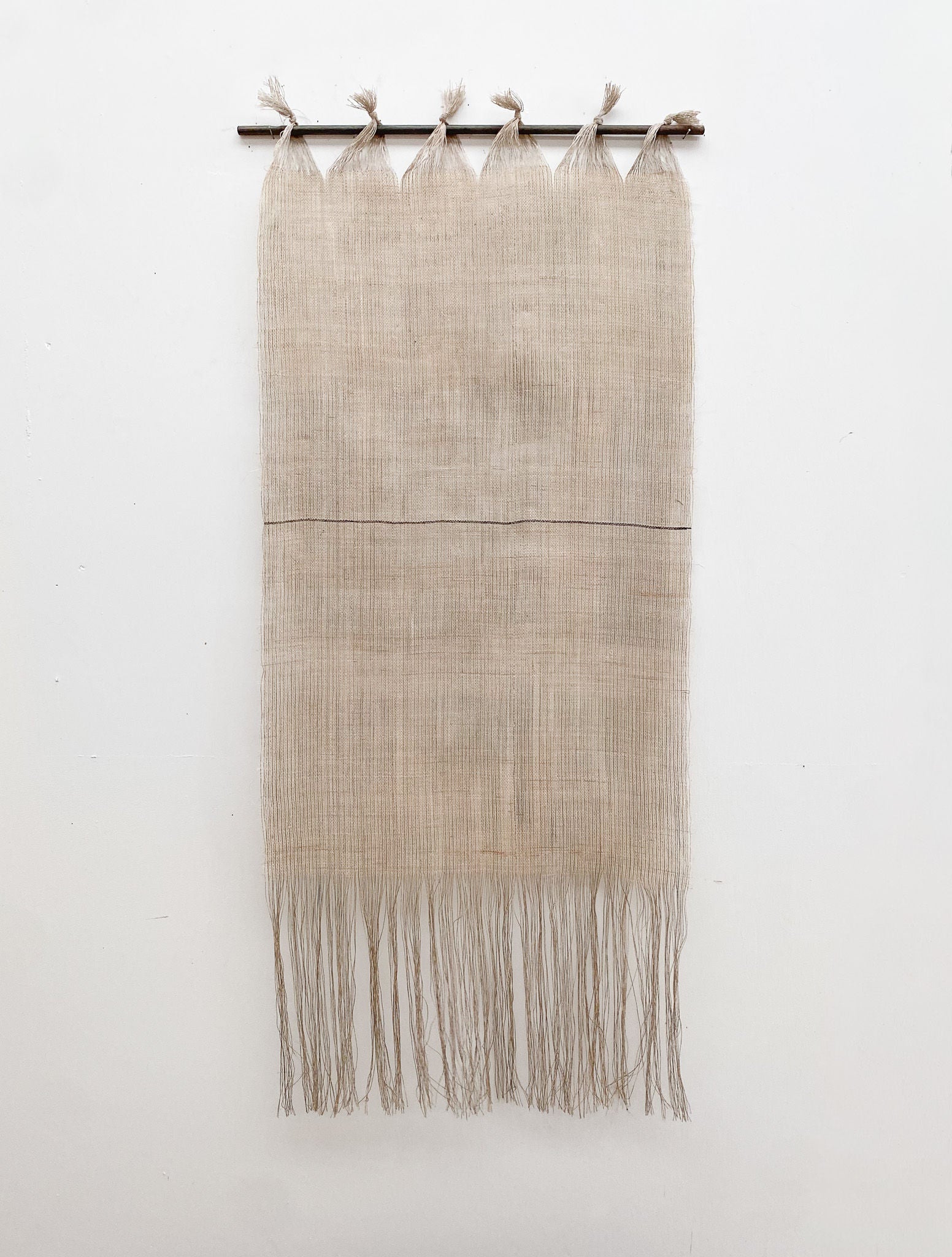 The Distant Horizon by Sundance Studio is a minimalist wall hanging featuring fine beige threads tied to a top rod, forming a loose weave that tapers into fringes on a plain white backdrop, evoking the wide open spaces of Yuraygir National Park.