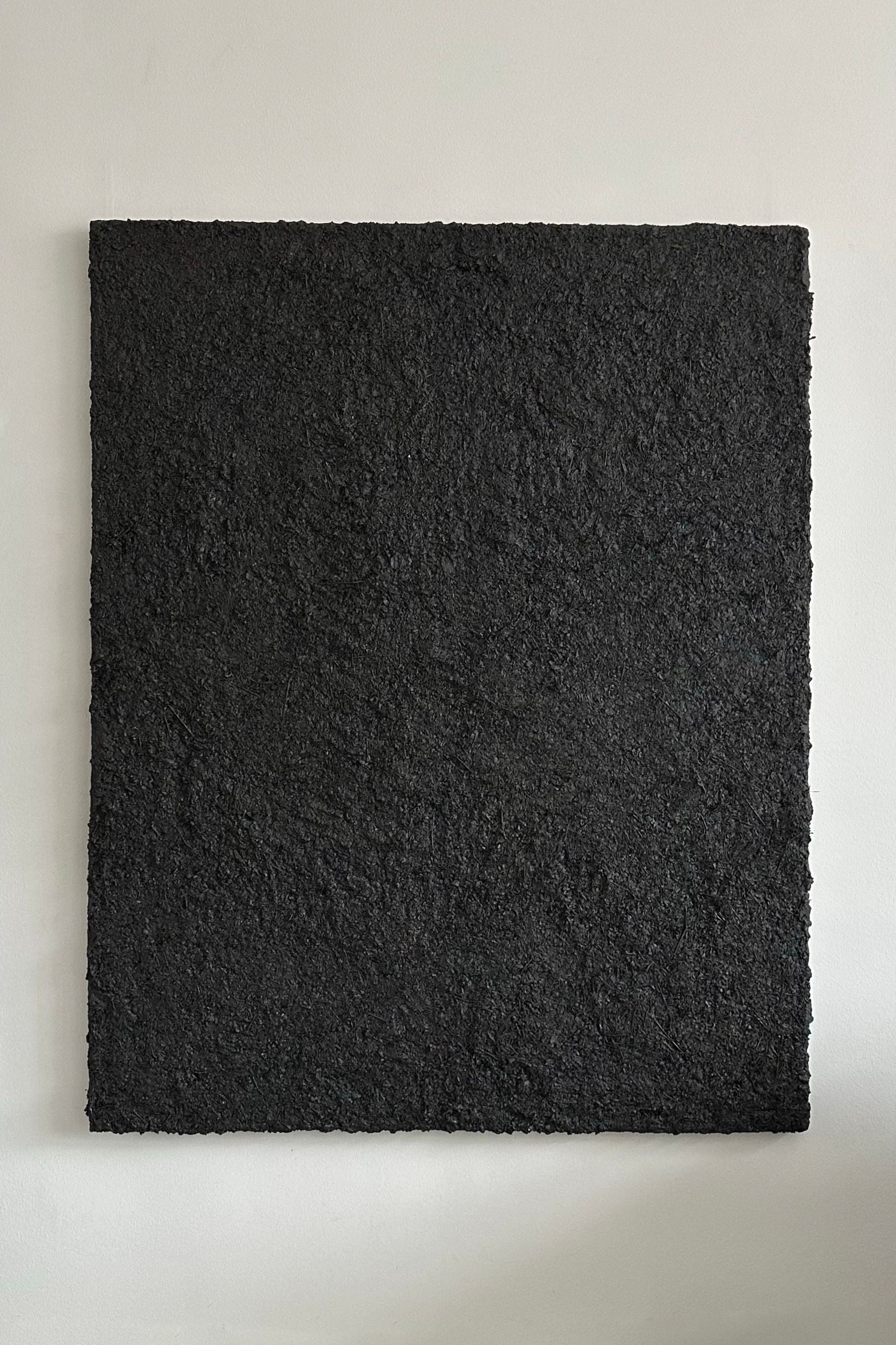 ‘ARCHE 06’ Sculptural Wall Art by CARRARA Studio, a large square piece with a textured black surface, hangs on a plain white wall. Its rough finish and subtle shading evoke raw, essential energy across the monochromatic work.