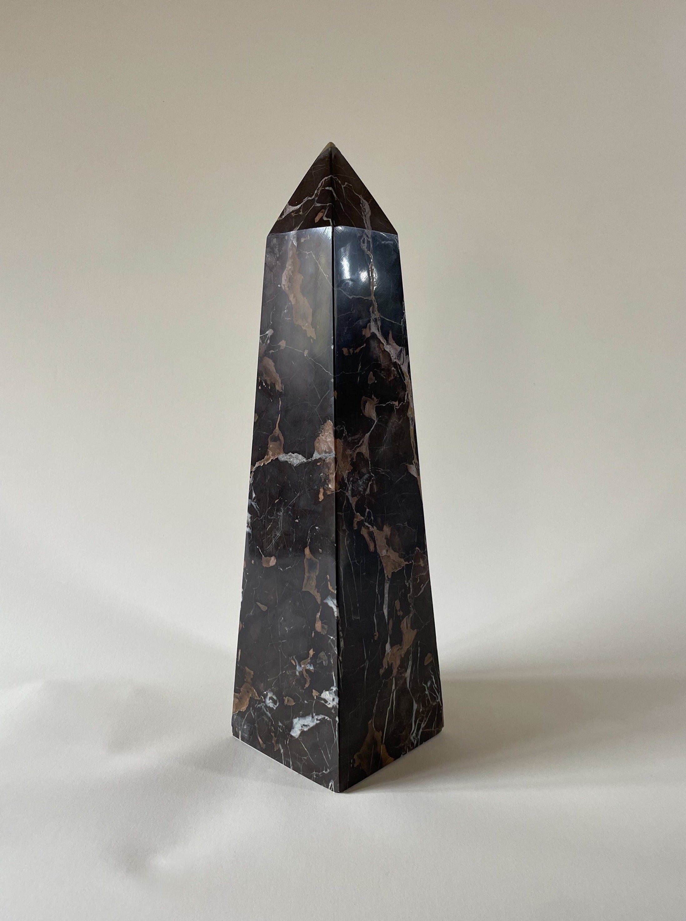A tall, polished Vintage Marble Obelisk by Maud Vaughan stands on a neutral background. The obelisk has a glossy surface with white, grey, and earth brown veining patterns running through it, giving it an elegant and sophisticated appearance.
