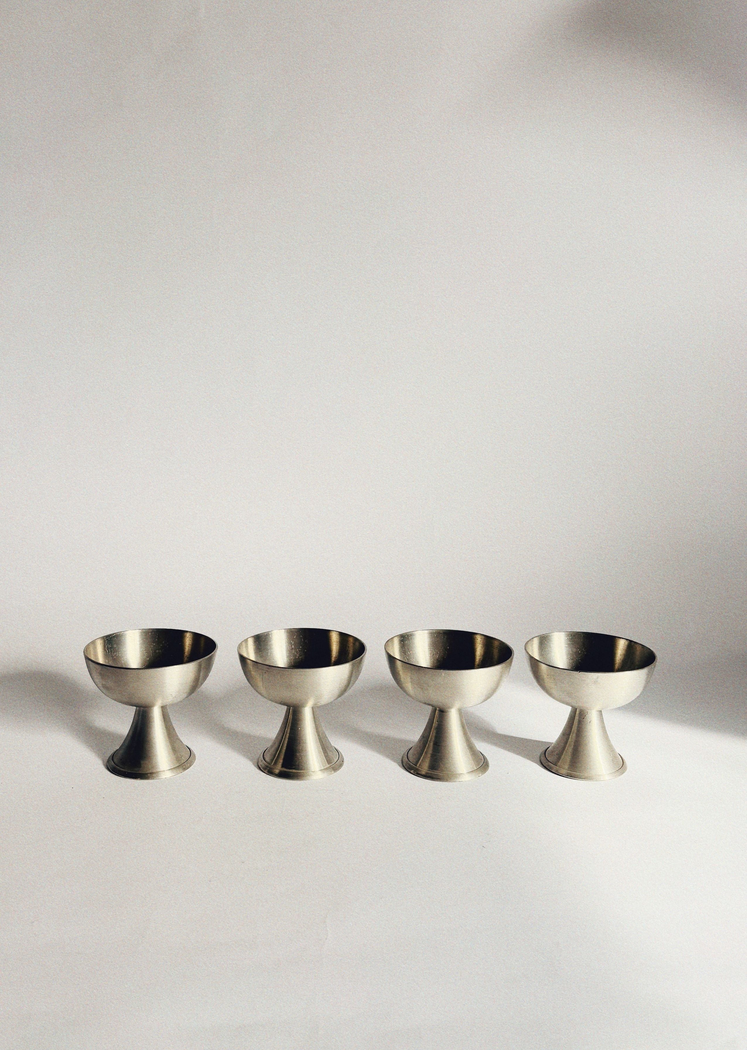 Set of four brushed brass dessert coupes on white surface