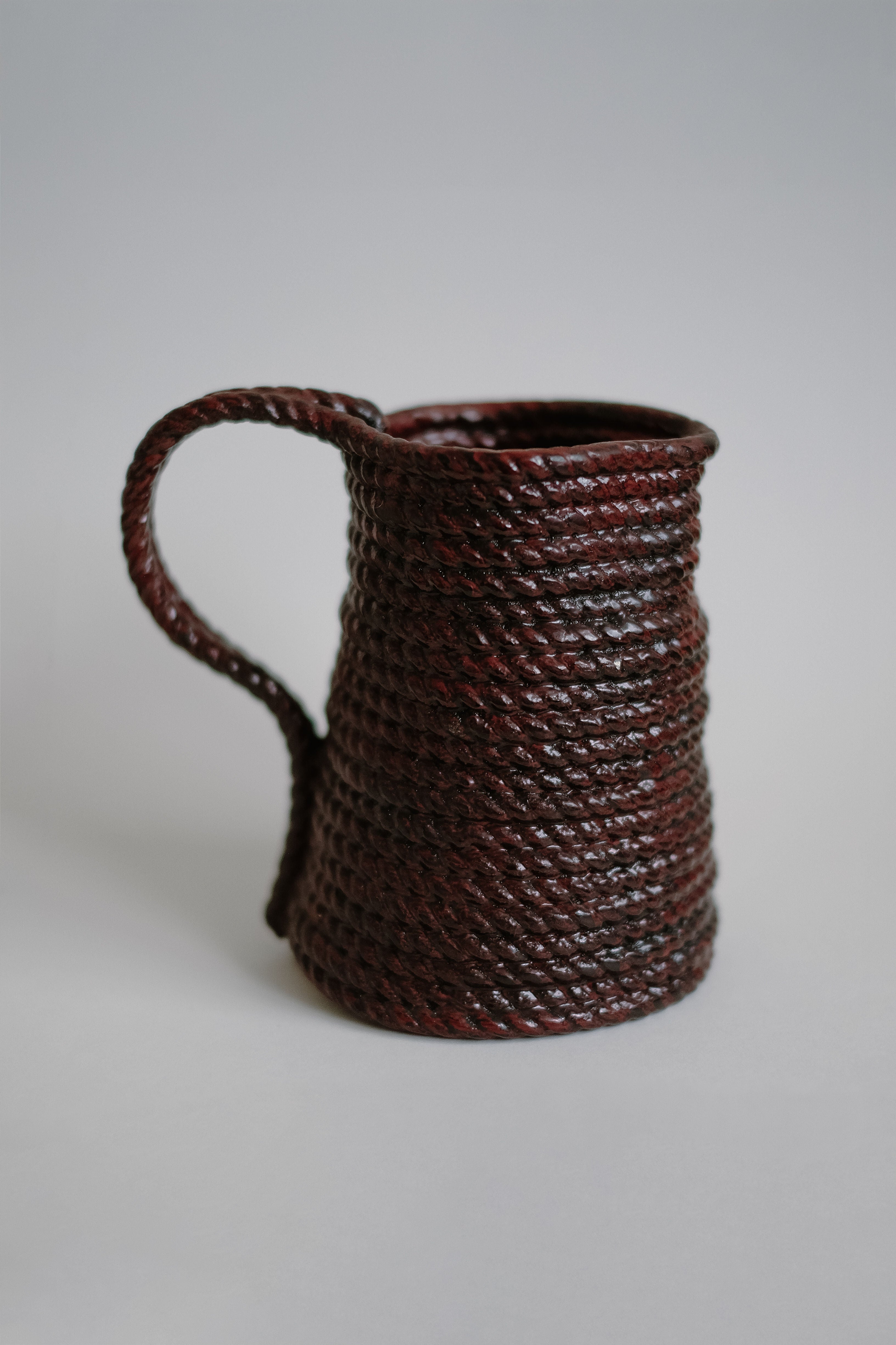 The Handmade Burgundy Vase by septembre studios features a textured, rope-like surface and a unique looped handle, displayed against a plain light gray background.