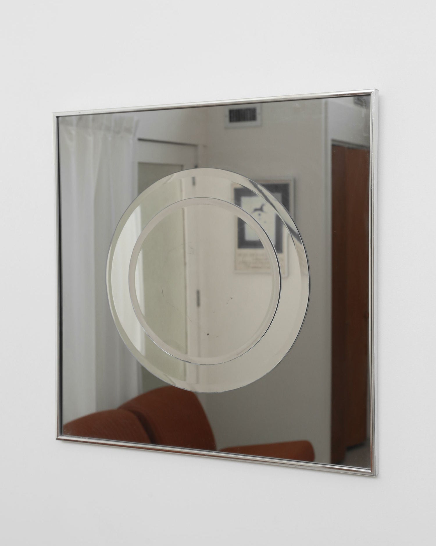 The Villa 1970’s Mirror is a square wall piece with a central circular frosted geometric design, reflecting a brown couch, white curtains, and framed art. This striking graphic mirror features a distinctive two-tone smoke effect.