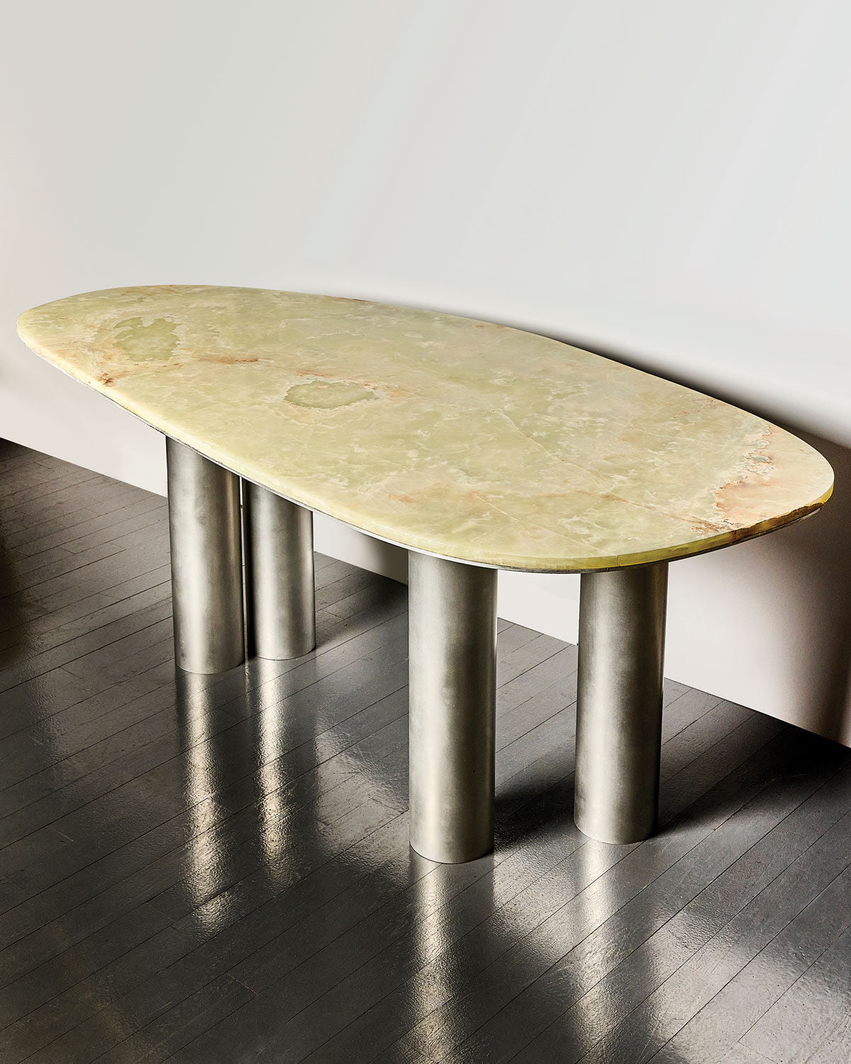 The Oni Desk in Green Onyx by Slash Objects features a large, uniquely shaped light green stone top supported by four handcrafted aluminum legs, shown here on a dark wood floor with a plain light background.