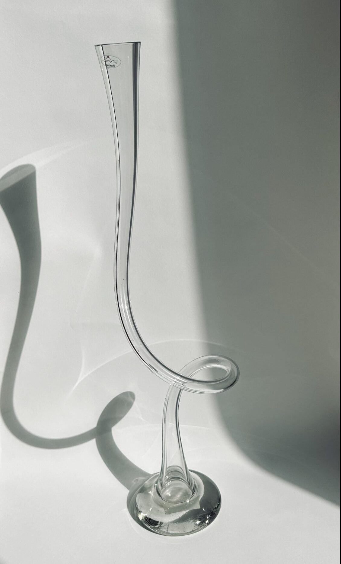 The large Swirl Vase from Flock Studio, handmade in the Netherlands, stands tall with an elegantly curved design. Its narrow opening and round base cast a soft shadow on any smooth surface, while the twisting neck adds an artistic flair to this decorative piece.