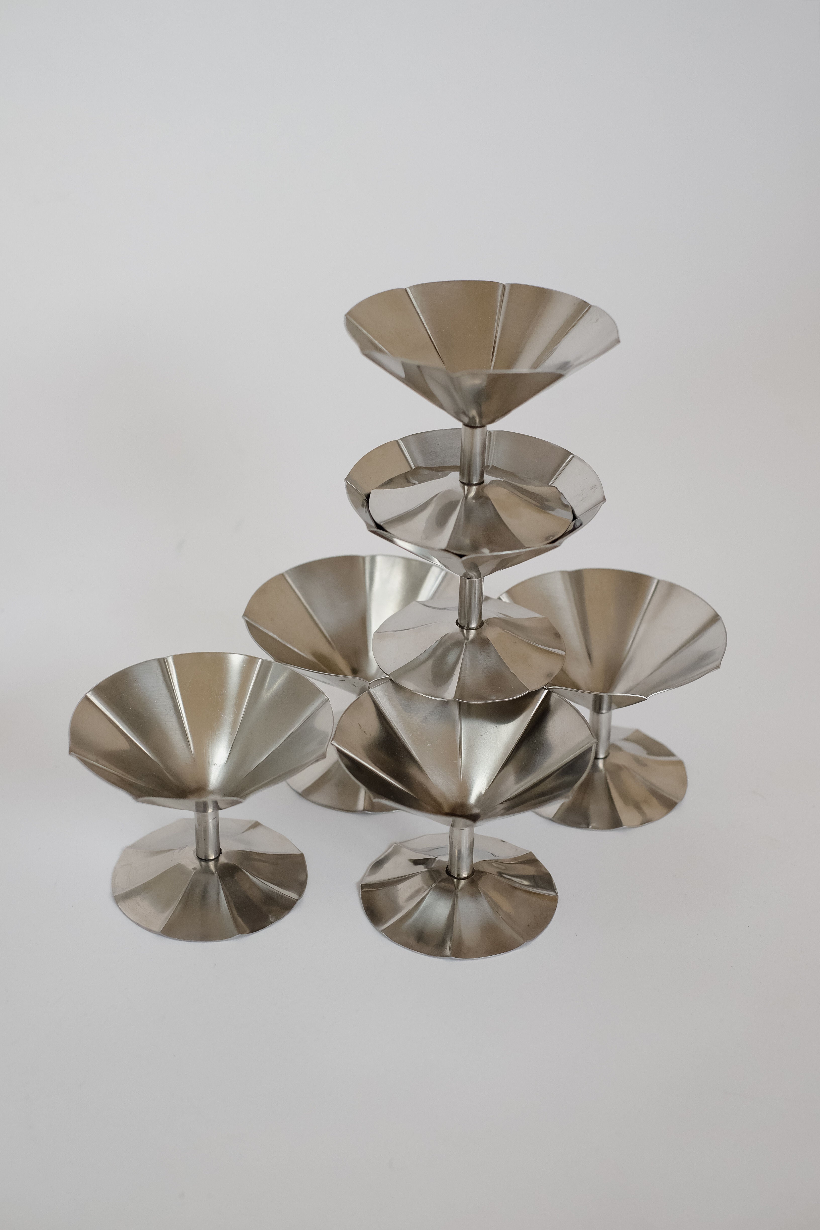 A pyramid of septembre studios' Set of 6 Ice Coupes, crafted in polished stainless steel, stands against a neutral backdrop. The reflective surface highlights the modern minimalist aesthetic.