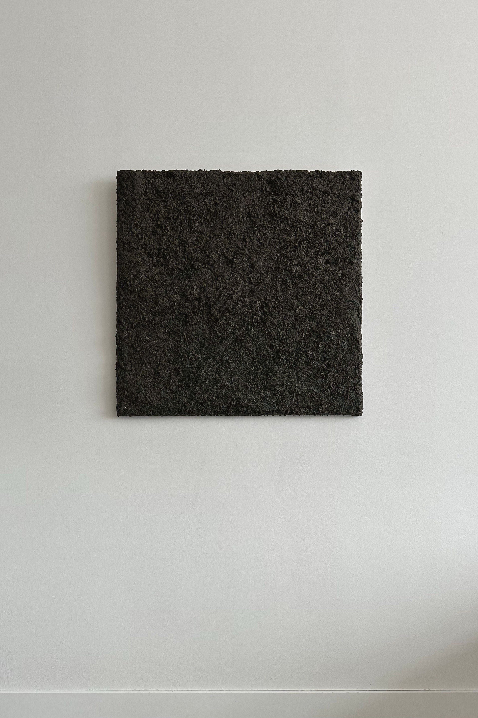‘ARCHE 07’ Sculptural Wall Art by CARRARA Studio—a rectangular, textured black piece—hangs on a white wall, its bold, raw surface evoking the primal energy of nature amid minimal surroundings.
