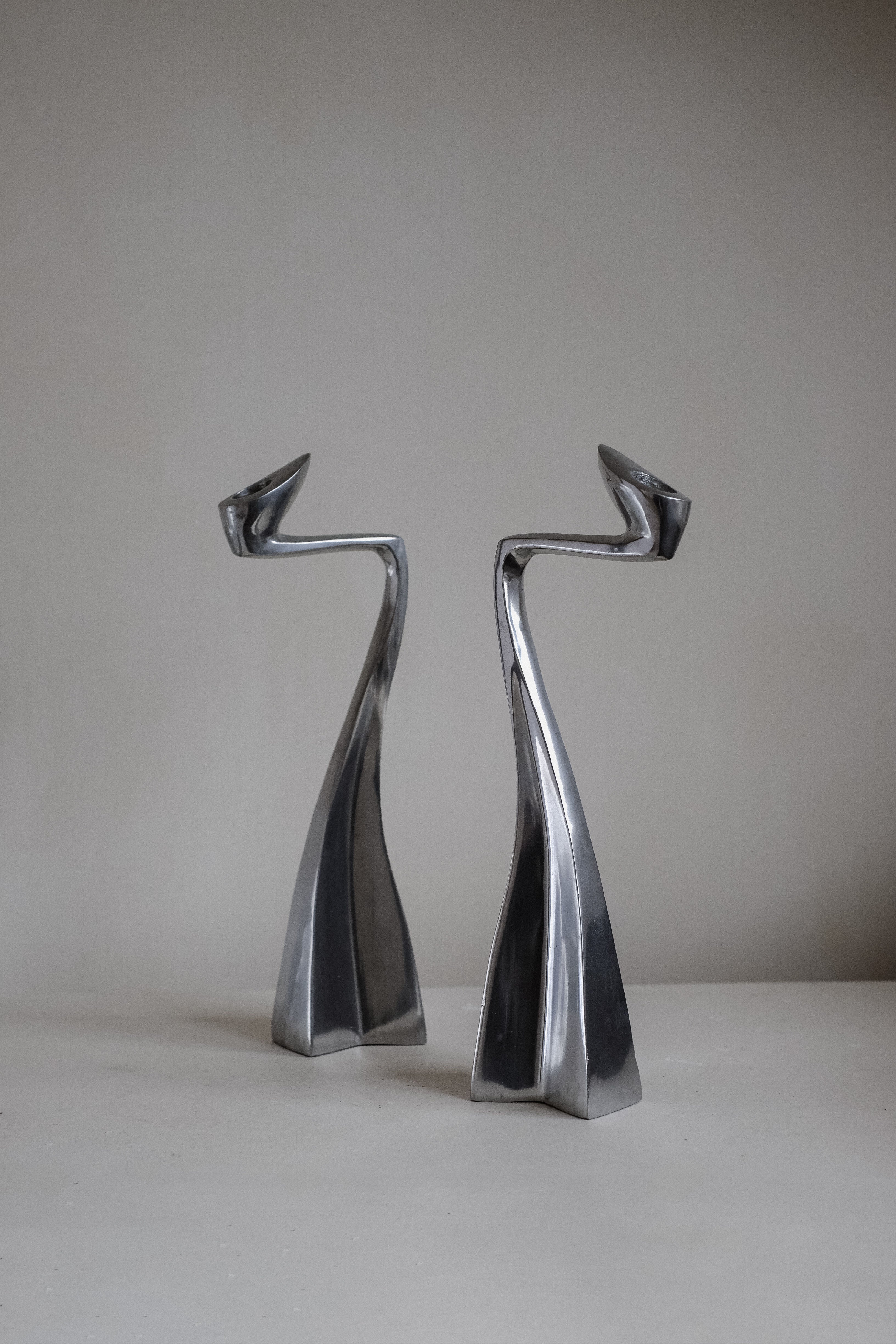 Against a neutral backdrop, two sleek candleholders by Matthew Hilton from the 80s feature smooth, twisting lines and pointed tops. These modern pieces from septembre studios add dynamic movement and make perfect collector's items for art enthusiasts.