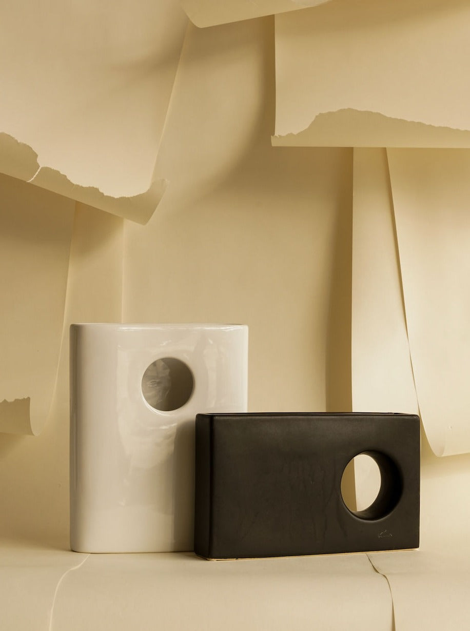 Two Contrasting Vases Set by Les Objets Amsterdam, one white and one black, displayed against a beige background with torn paper textures.