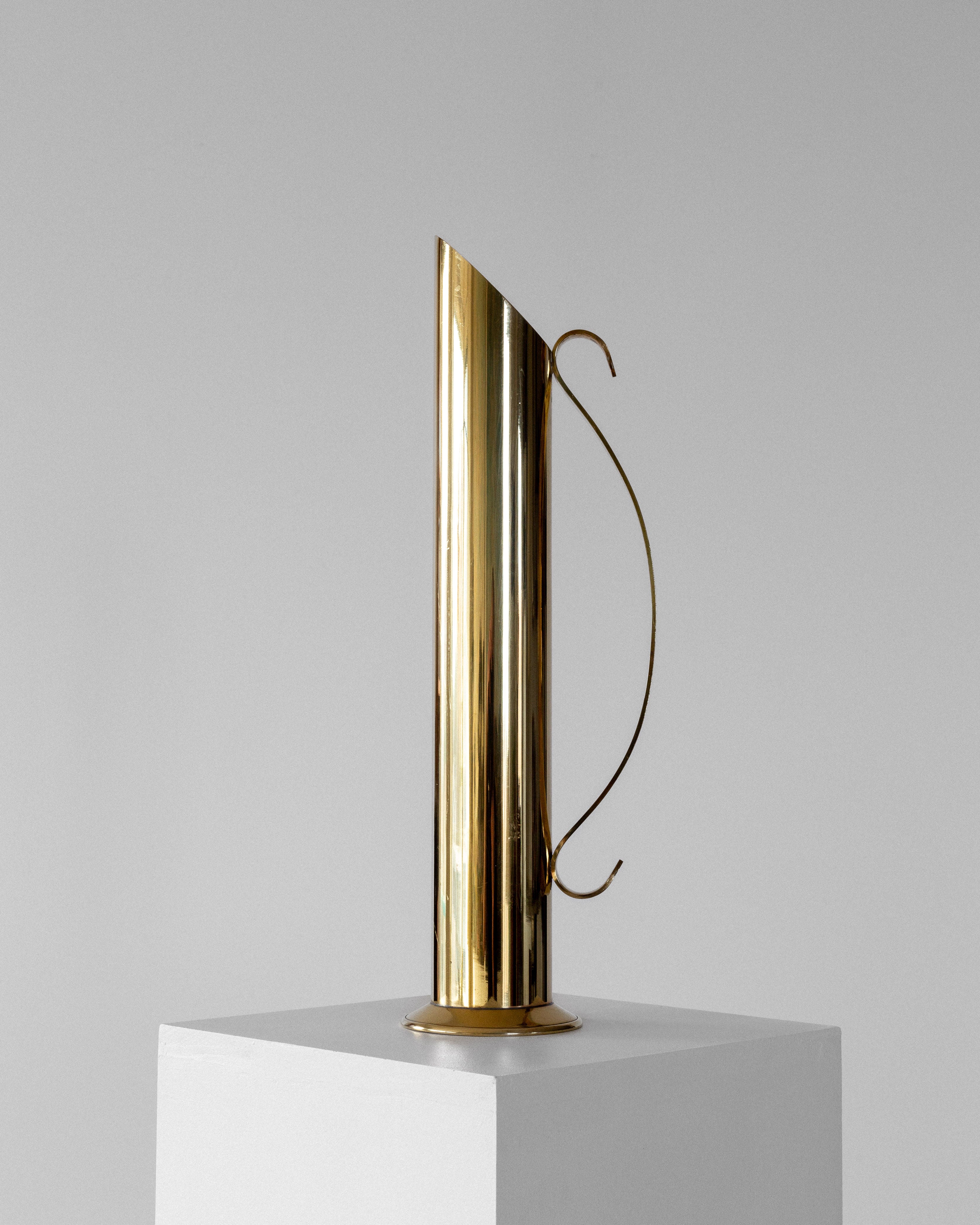 The Spigel Large Mid-Century Brass Vase, featuring a tall, minimalist design with a narrow spout and thin curved handle, is displayed on a white pedestal against a plain gray background.