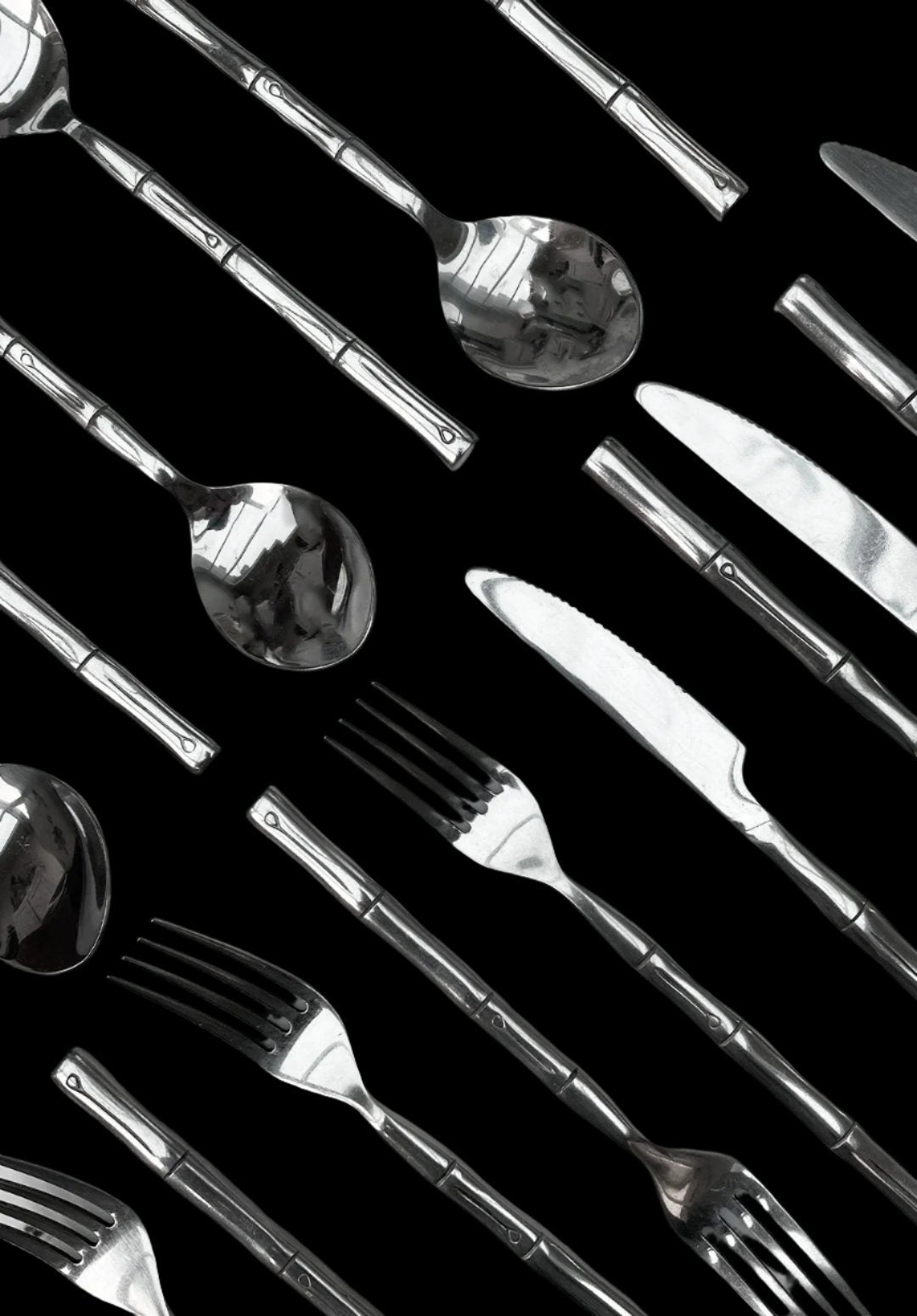 A set of bamboo cutlery from Les Objoies, featuring knives, forks, and spoons, arranged diagonally on a black background. The utensils showcase a sleek, modern design with a subtle pattern on the handles and have a shiny finish.