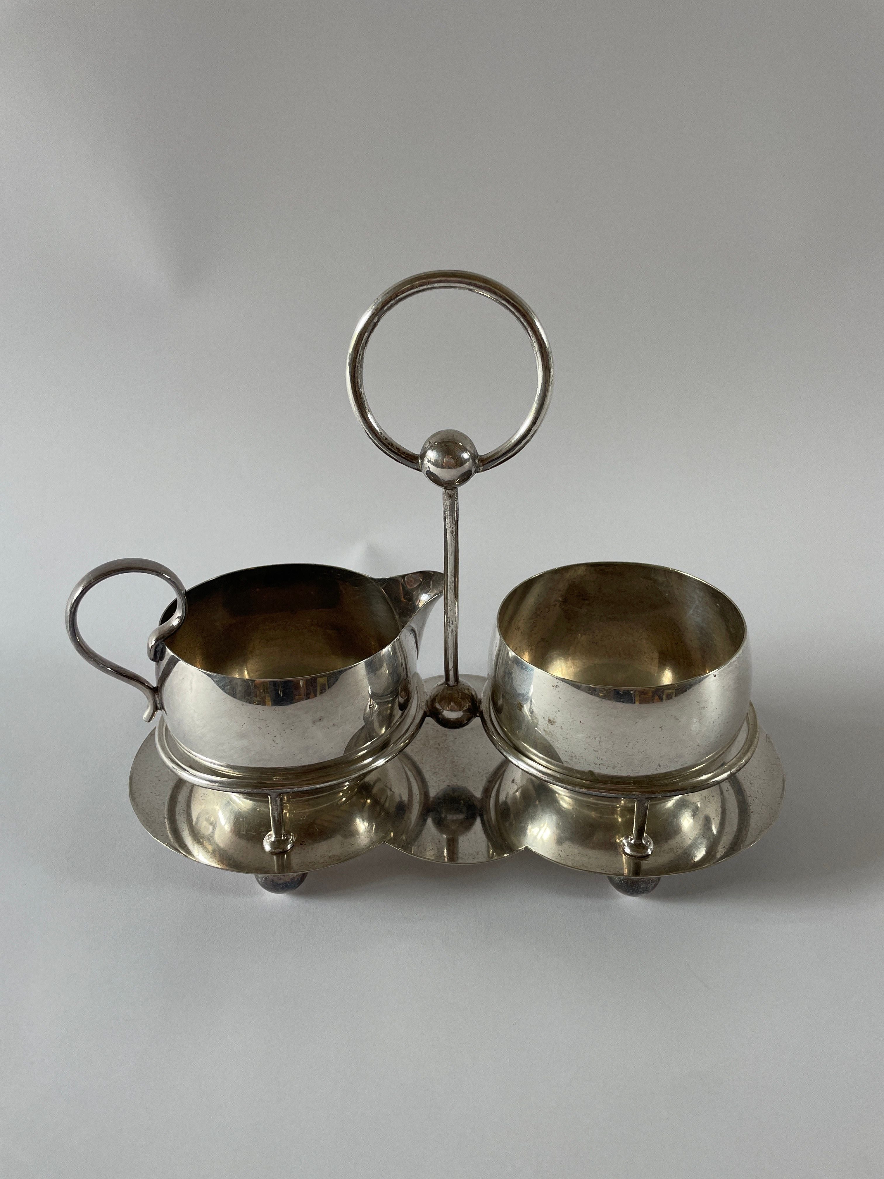An Antique Silver Plate Tea Service Set by Maud Vaughan from the UK, circa 1910, elegantly adorns a small tray with a circular handle. The sleek, reflective surfaces of the pitcher and matching open bowl add an elegant touch to any setting.