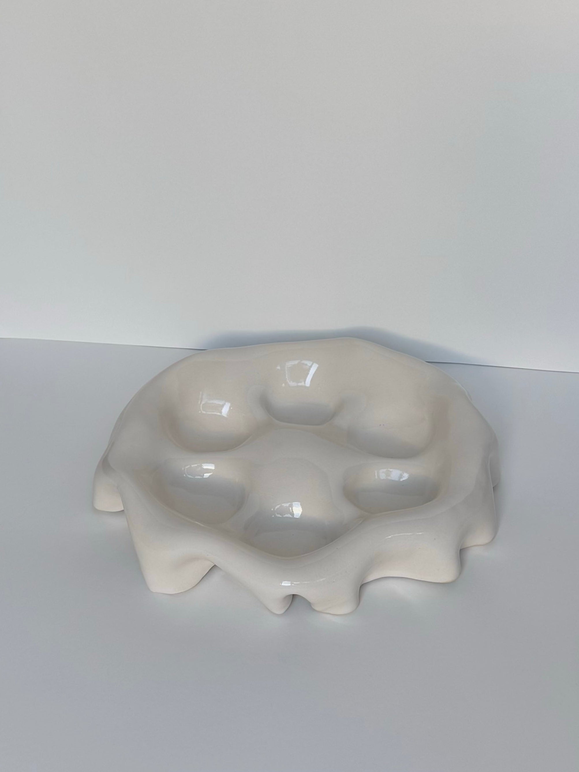 The Goobs Ceramics Snack Plate is a glossy white, hand-made stoneware tray with an irregular, wavy edge. Its high gloss glaze forms five round, melted-like indentations on a plain background.