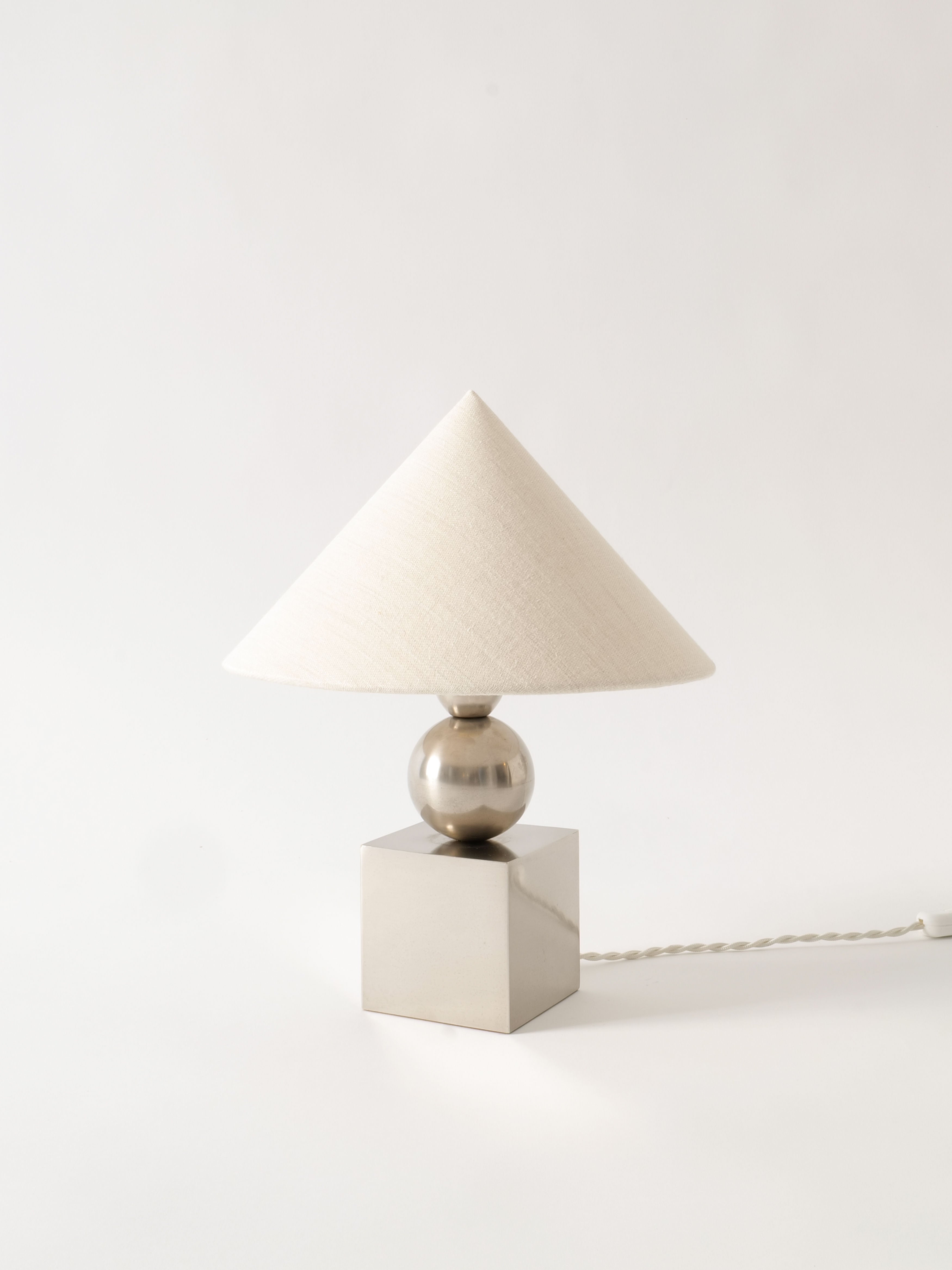 A Barbier Sculptural Lamp 1970s by Collection apart with a conical white shade, a chrome over brass spherical core, and a square metal base. The lamp's power cord extends to the right, blending into the white background.