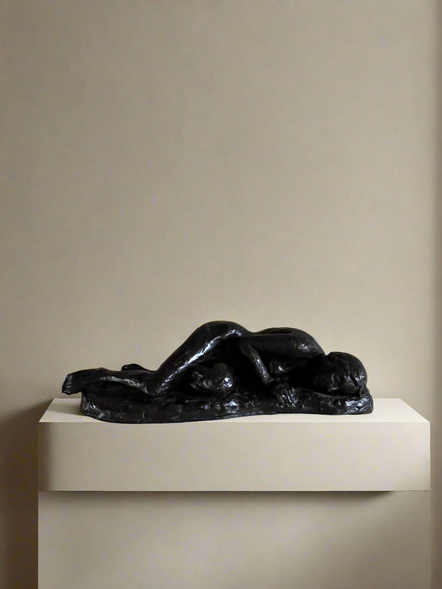 A plaster sculpture of a reclining, resting nude by Maud Vaughan graces the display pedestal against a plain, beige backdrop. The figure is elongated, with a smooth, flowing form that captures a serene and tranquil pose.