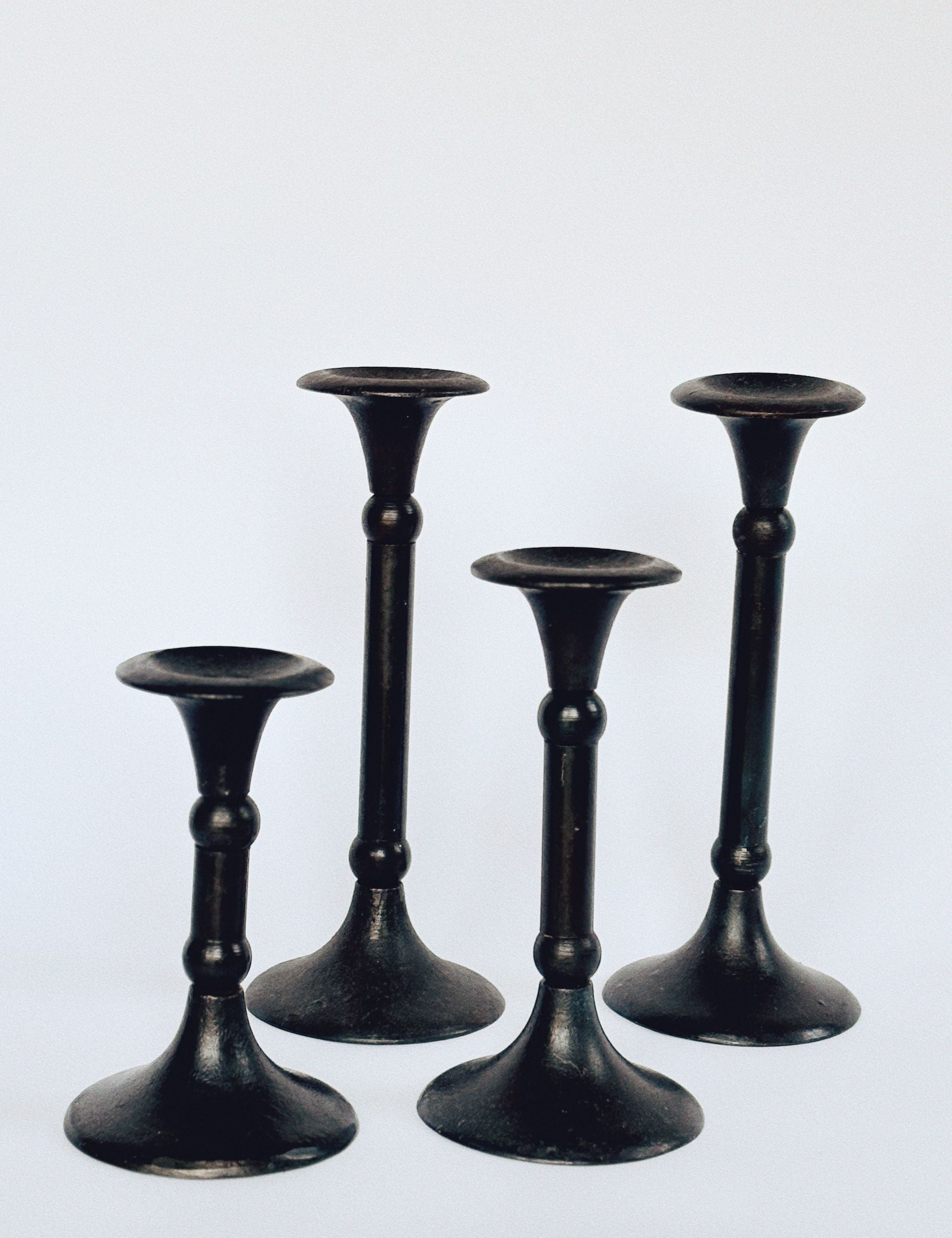 The Huerto Set of 4 Cast Iron Candleholders, displayed on a white background, features heavy vintage pieces with simple elegant designs. Each has a wide base, narrow stem that flares at the top, and subtle ball details for secure candle placement.