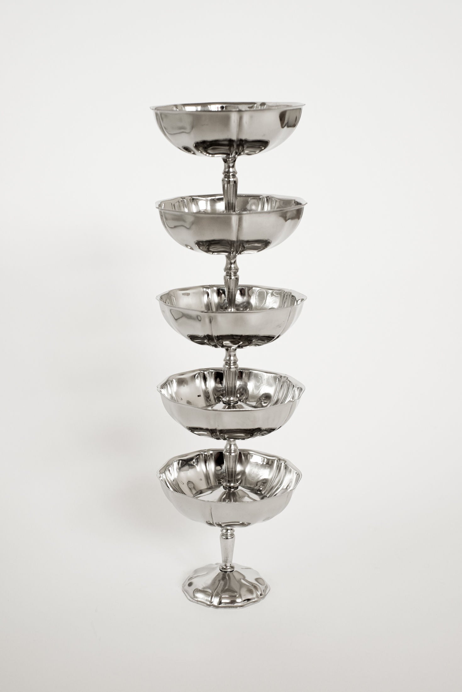 A vertical stack of the Set of Five Ice Coupes by septembre studios, crafted from shiny stainless steel and arranged against a white background, creates a striking and vintage-inspired display.