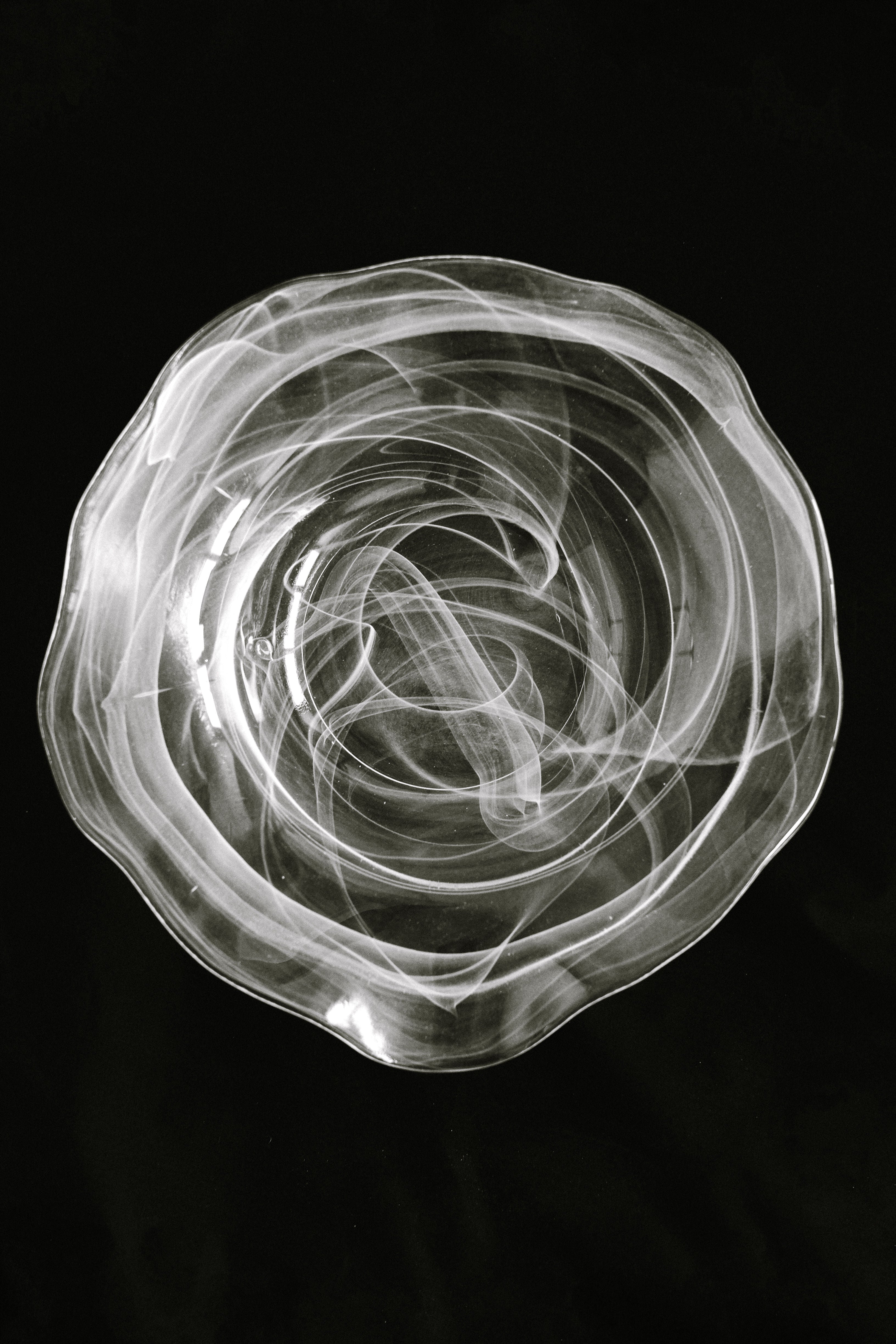 The septembre studios Swirl Glass Bowl, featuring medium-large dimensions and exquisite craftsmanship, sits against a black background with dramatic wavy, swirled patterns for an abstract effect.