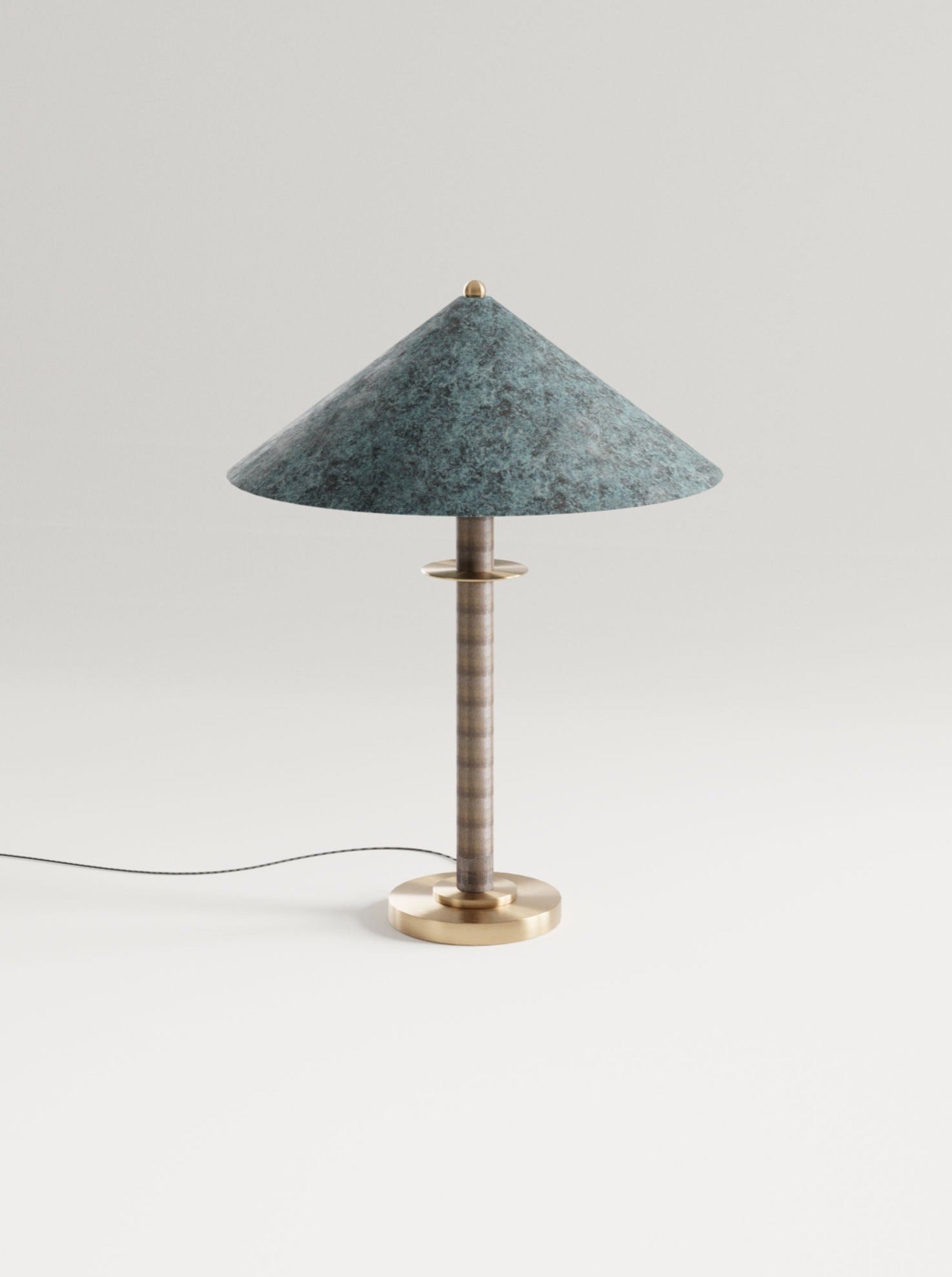 A stylish Louisa II Table Lamp by Marine Breynaert with a broad brass shade in blue-green and a segmented solid bronze stem, placed on a white background. The lamp's cord trails off to the side.